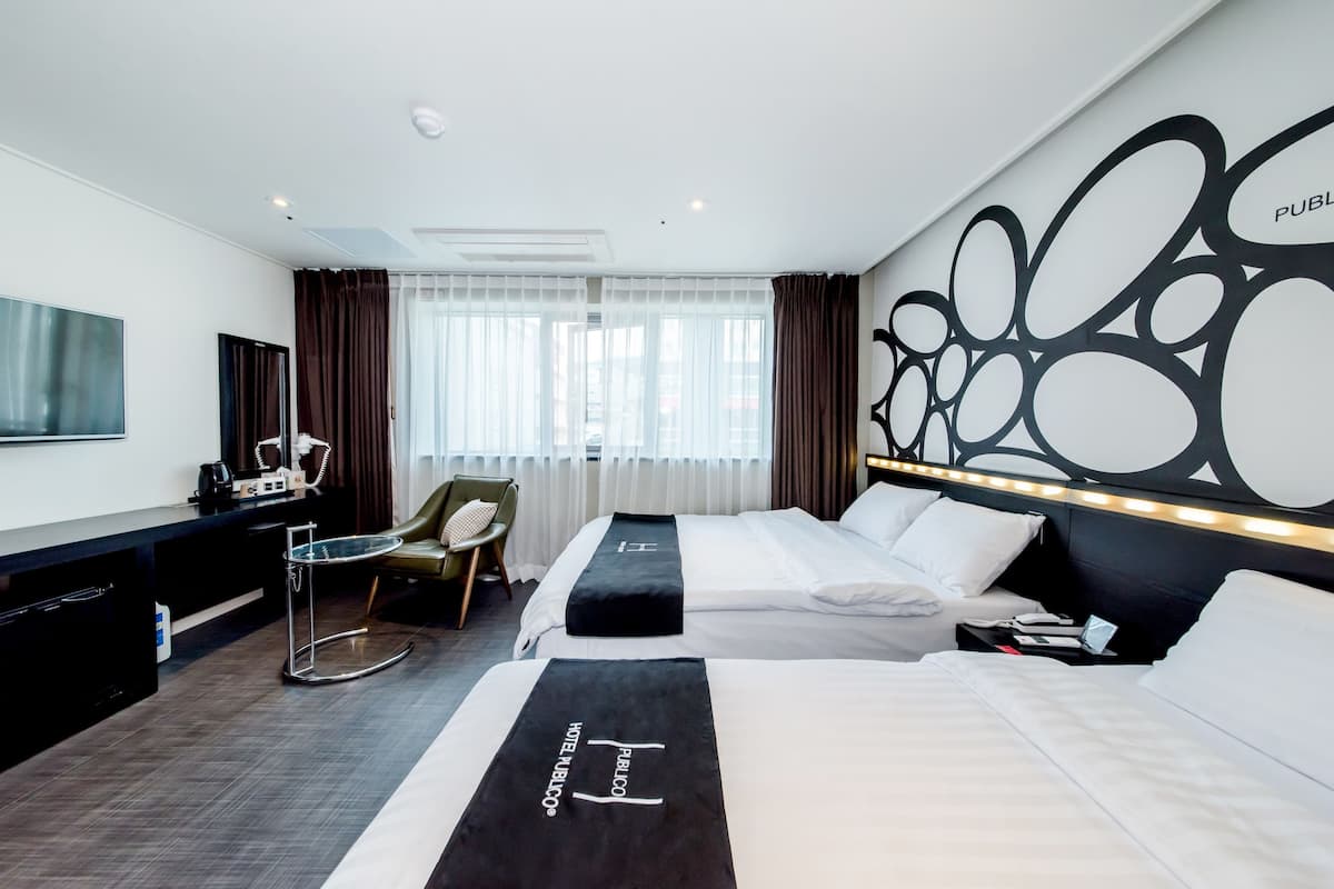 Una habitación de hotel con dos camas, un escritorio, una silla, un televisor y un adorno en la pared.