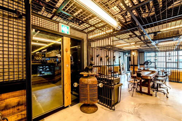 Un interior espacioso con techo alto, iluminación de estilo industrial y una zona de estar central con mesas y sillas.