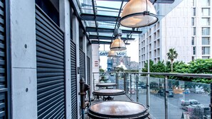 Une terrasse sur le toit, avec des tables et des chaises, une rambarde en verre et une vue sur le paysage urbain.