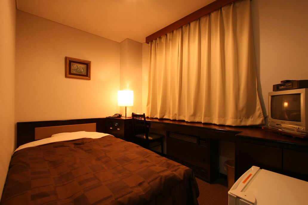 A hotel room with a bed, desk, chair, television, and a lamp.