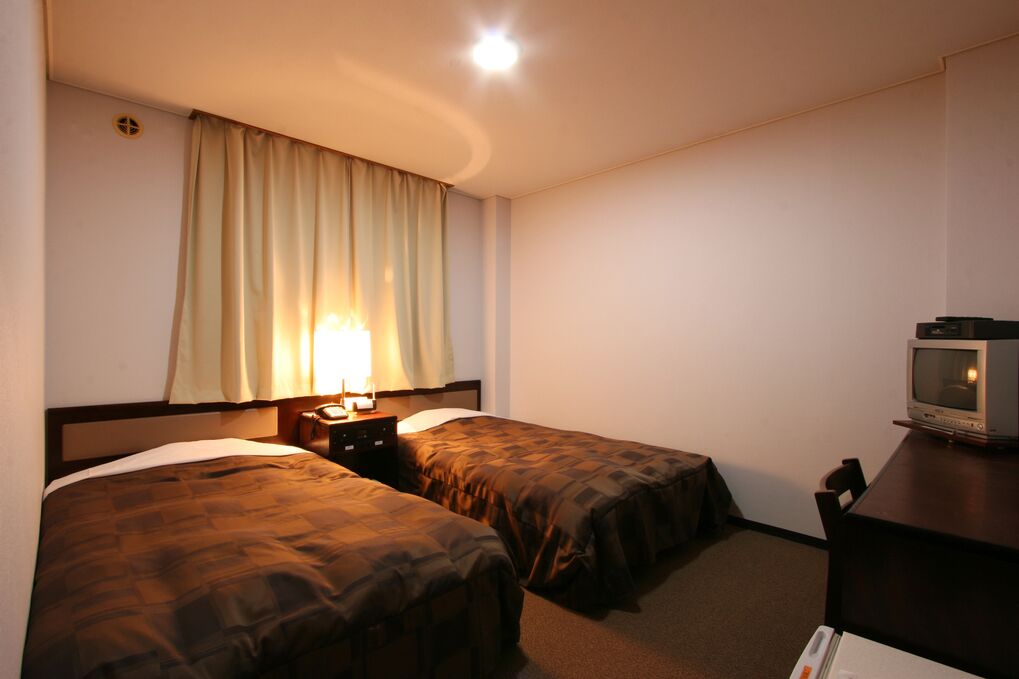 A hotel room with two beds, a TV, a desk, and a lamp.