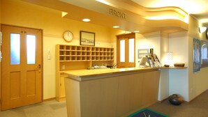 A reception area with a wooden reception desk, a clock, a framed picture, and a sign labeled "FRONT". - Hotel Ekimae (Hakodate)