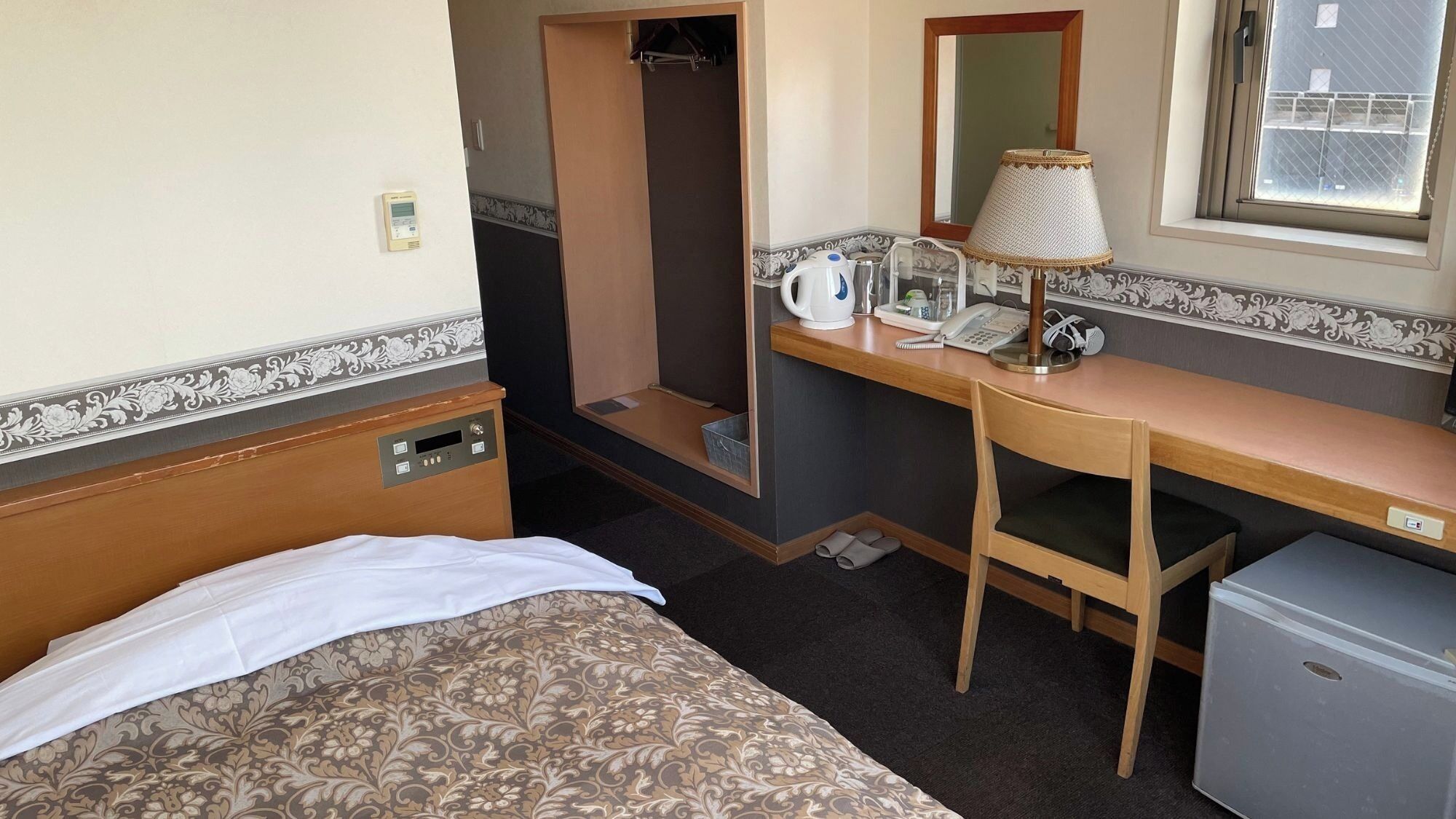 Een hotelkamer met een bed, een bureau met een lamp, een telefoon en een kleine koelkast.