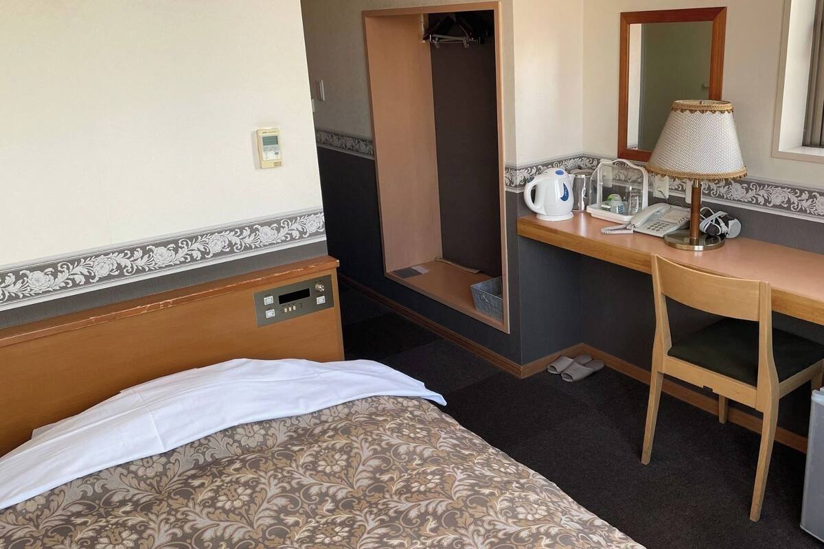 Een hotelkamer met een bed, een bureau met een lamp, een telefoon en een kleine koelkast.