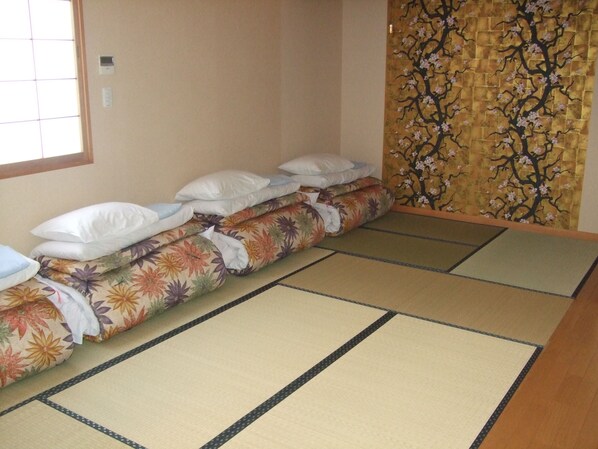 A tatami mat room with a low bed, pillows, and a decorative wall. - Hotel Ekimae (Hakodate)