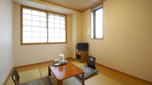 A room with tatami flooring, a low table with a kettle, a chair, and a television on a stand. - Hotel Ekimae (Hakodate)