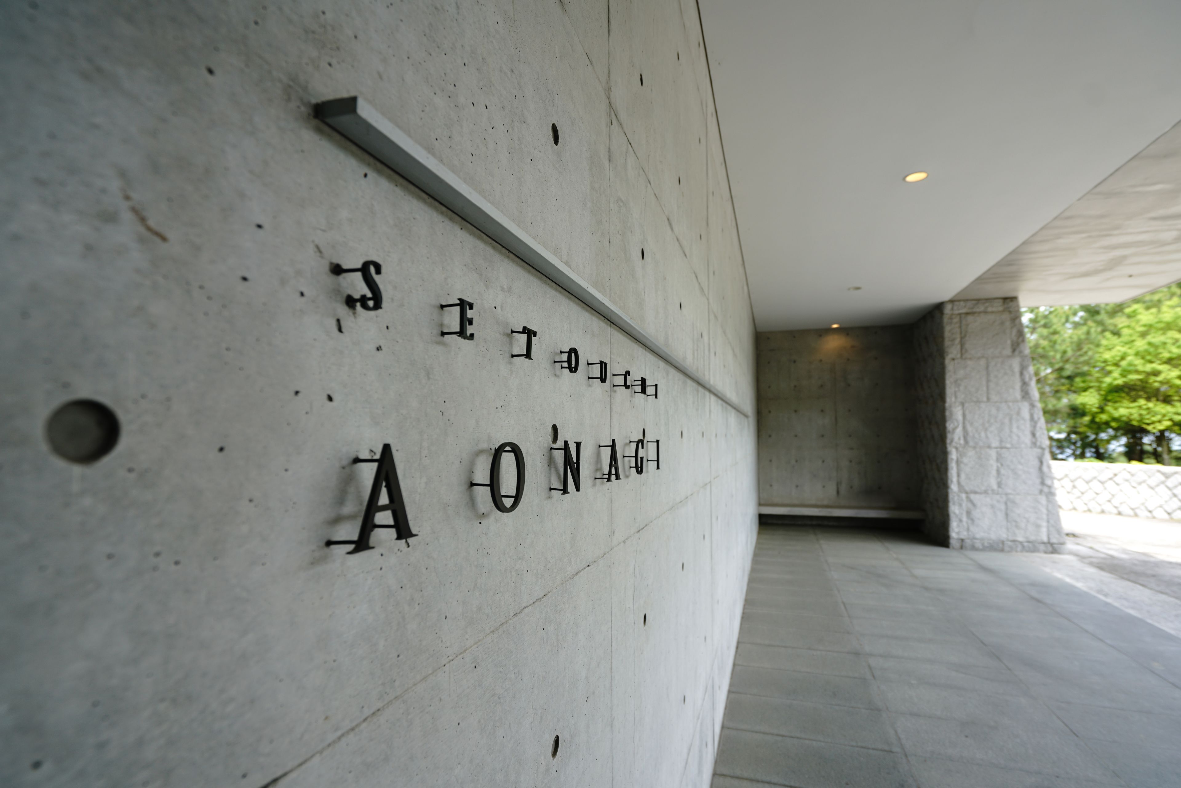 A concrete wall with engraved text, a recessed ceiling, and a stone pillar.
