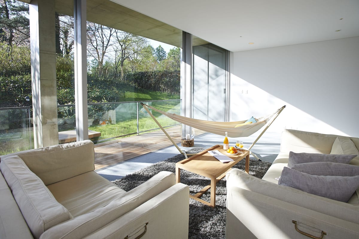A modern living room with a large glass window, a hammock, and a wooden coffee table.