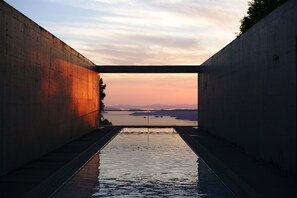 A concrete structure with a reflective water surface leading to a body of water, surrounded by a natural landscape. - SETOUCHI RETREAT AONAGI by Onko Chishin (Matsuyama)