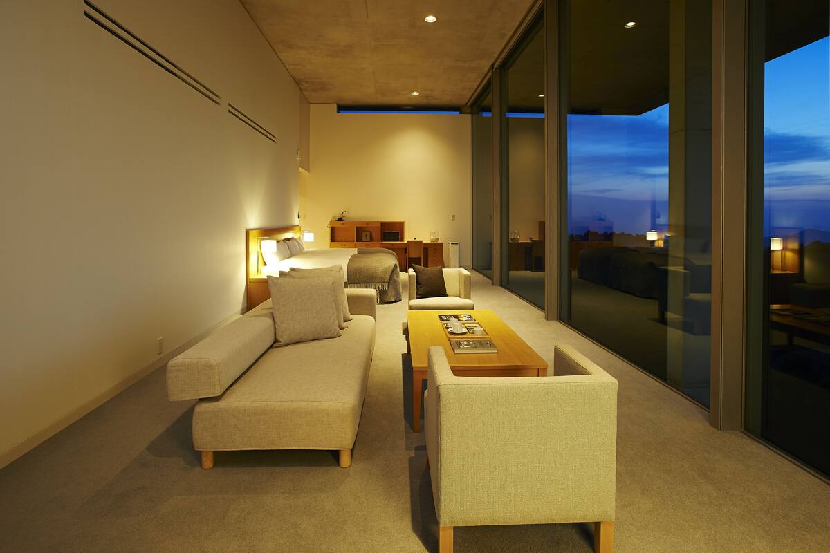 A modern living room with a sofa, armchairs, a coffee table, and a desk with a lamp.