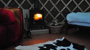 Ein gemütliches Zimmer mit Kamin, einem roten Sessel, einem Bett und einem Kuhfellteppich.
