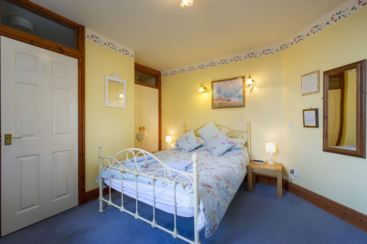 A bedroom with a bed, bedside tables, a mirror, and a painting on the wall.