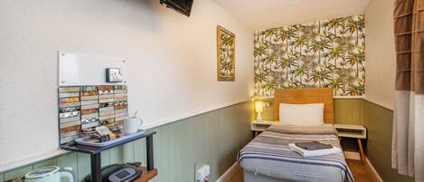 A compact hotel room with a bed, a desk with a kettle, a television, and a patterned wallpaper.