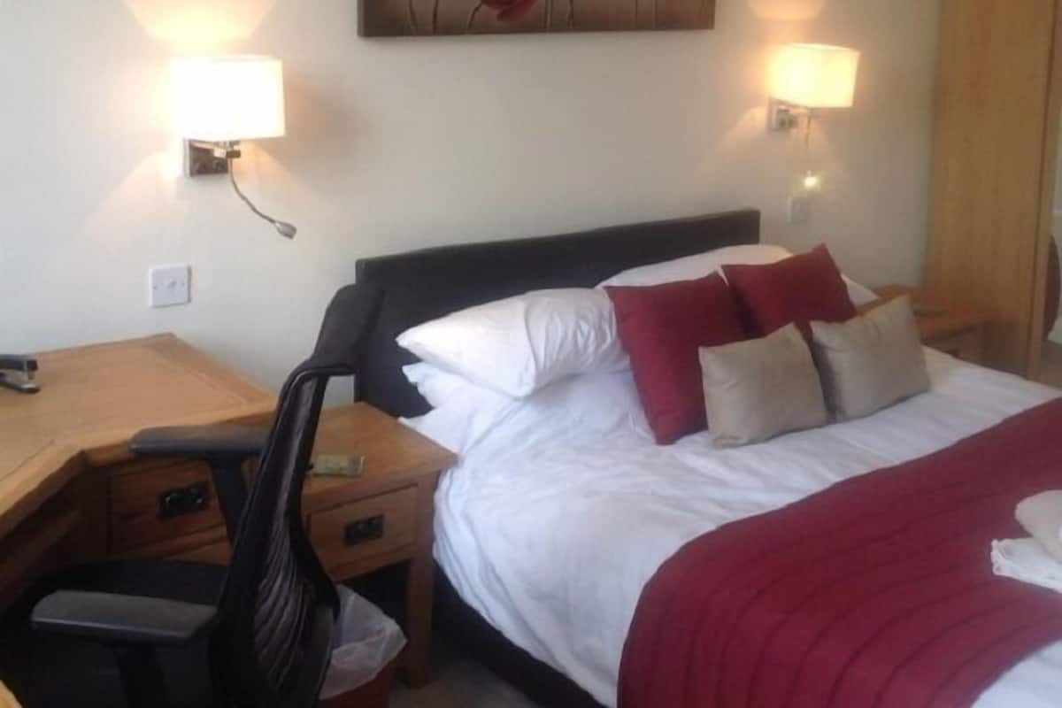 A hotel room with a bed, bedside lamps, a desk, and a chair.