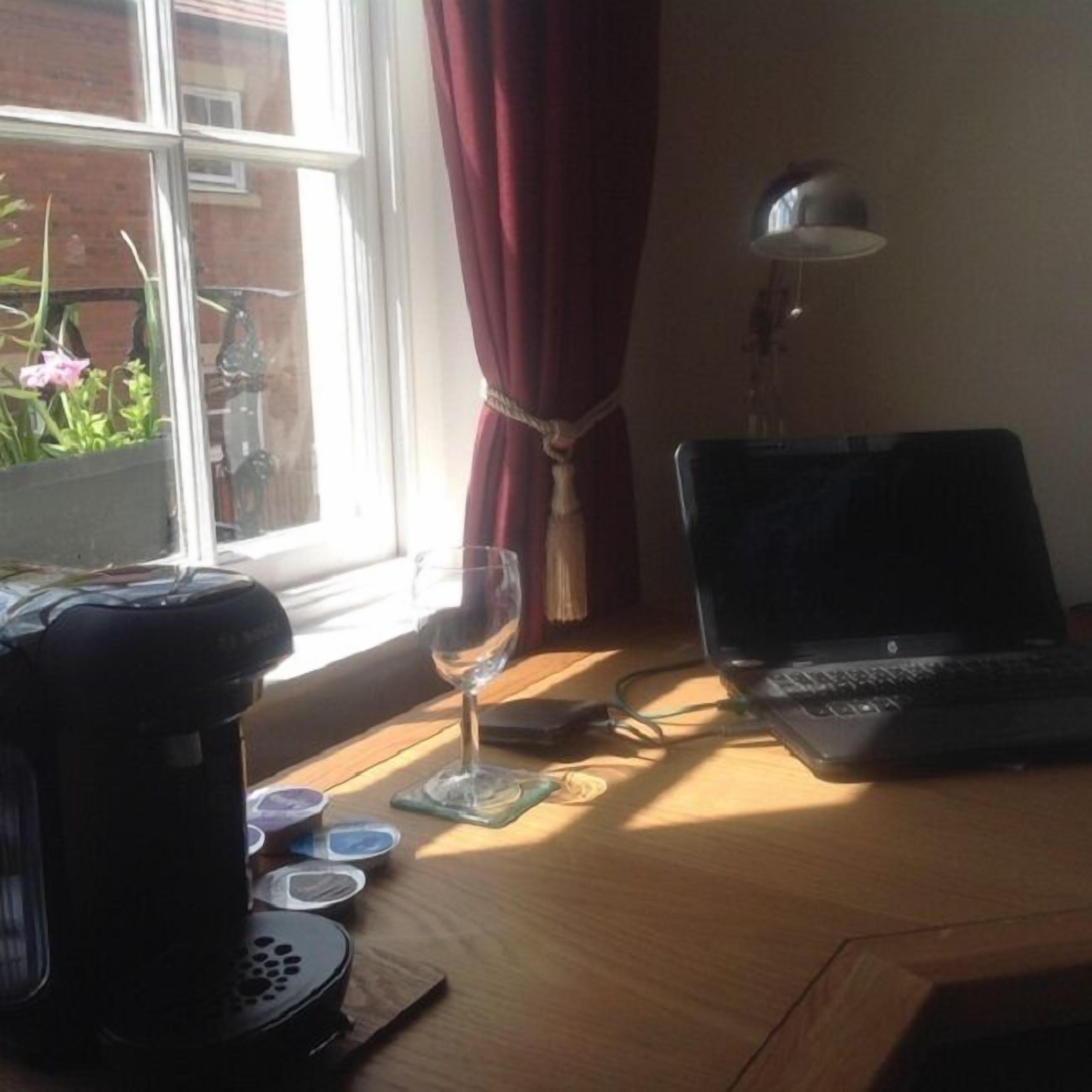 A wooden desk with a laptop, a glass of water, and a coffee maker.