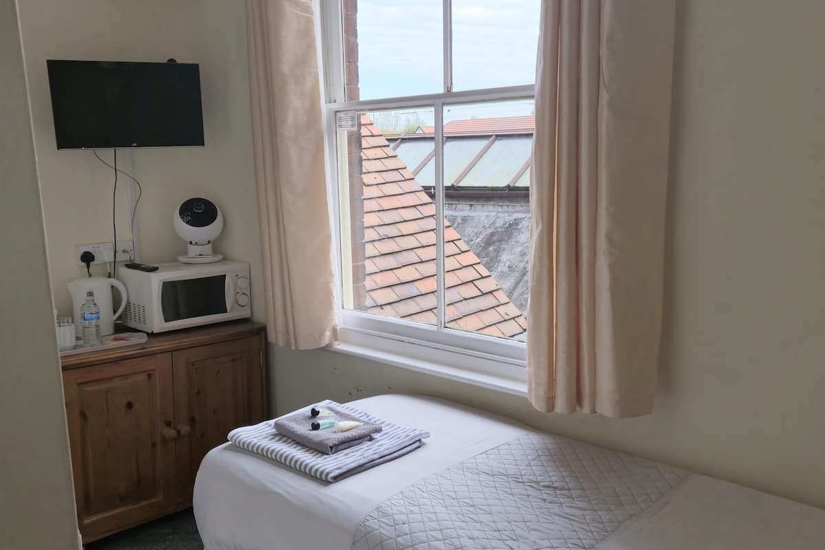 A bedroom with a bed, a TV, a microwave, a cabinet, and a window with curtains.