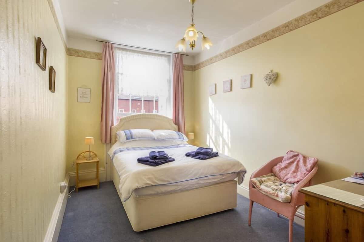 A bedroom with a bed, a chair, a desk, a lamp, and a window with curtains.