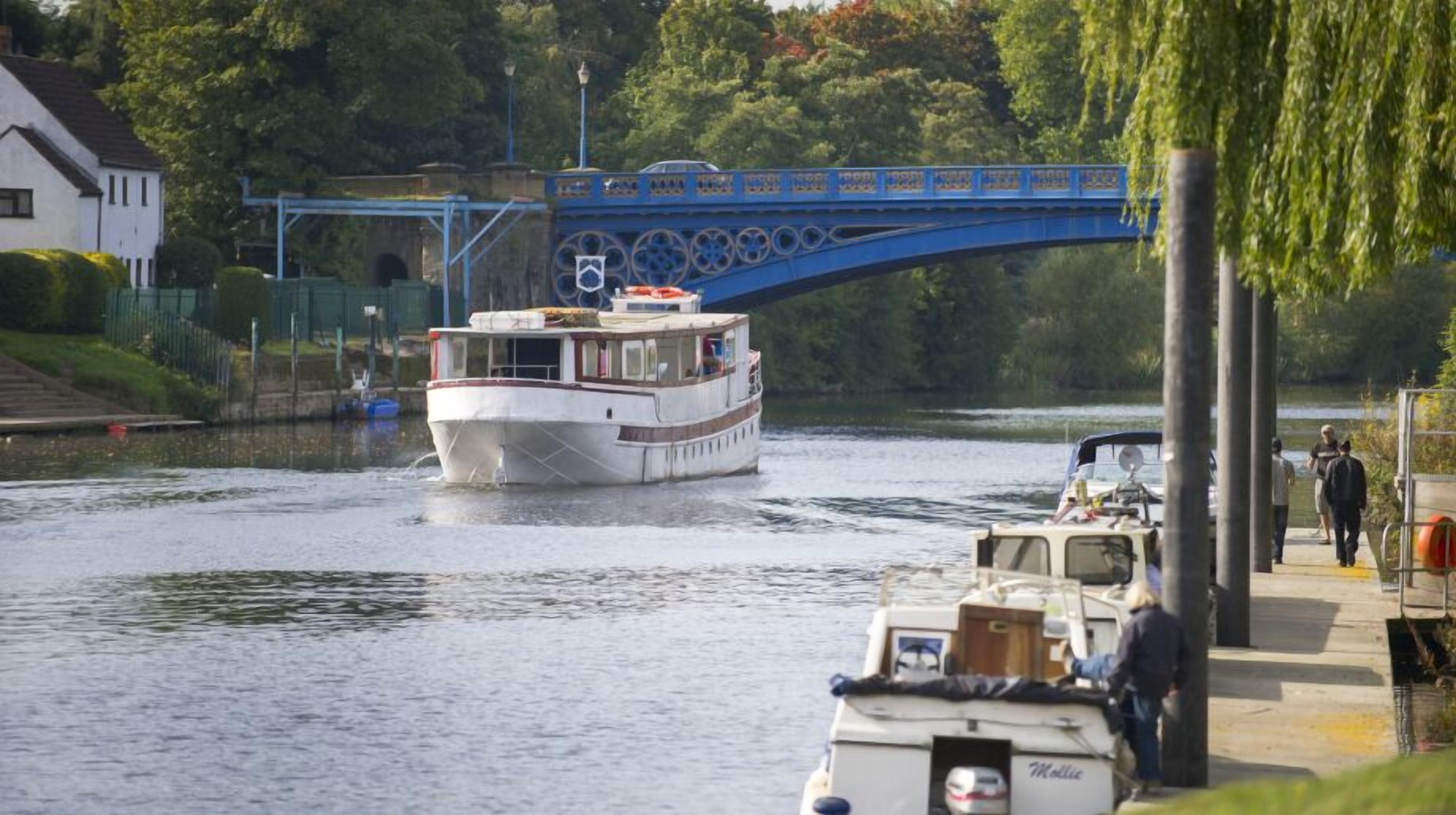A river with a white boat and a blue bridge in the background.