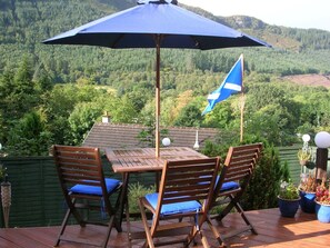 Eine Terrasse mit Tisch und Stühlen, eine Flagge und Blick auf ein bewaldetes Tal.