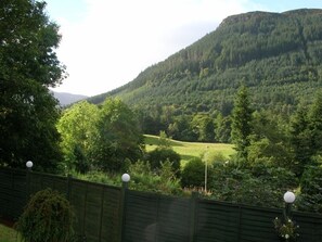A view of a lush green valley with a wooden fence and lamp posts in the foreground.