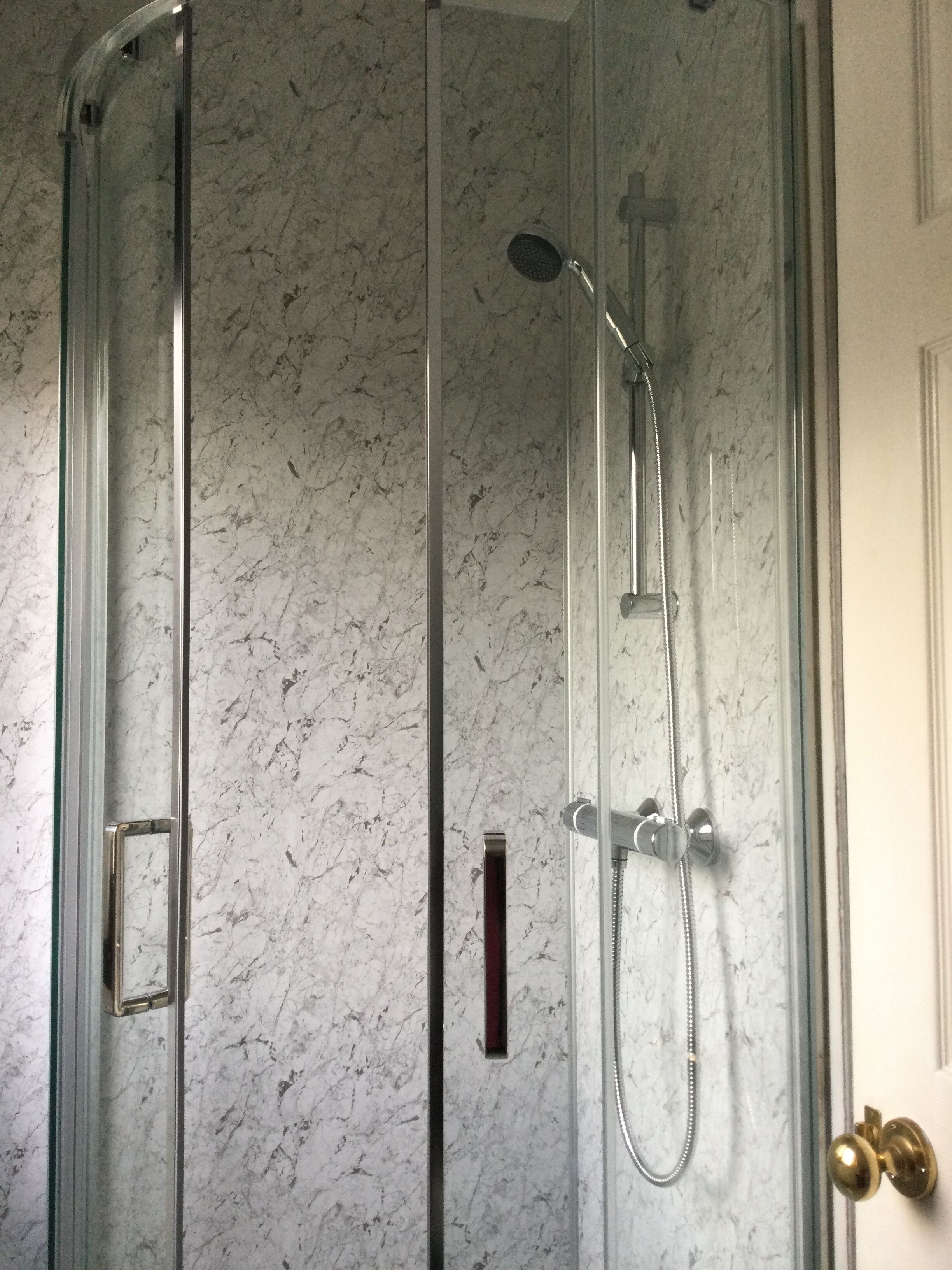 A glass-enclosed shower with a handheld showerhead and a wall-mounted faucet.