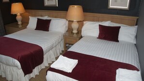 Habitación de hotel con dos camas, cada una con ropa blanca y una manta roja. Hay dos lámparas de noche sobre mesitas de madera.