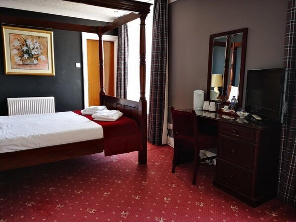 A hotel room with a four-poster bed, a desk with a mirror, and a television. - Caledonian Hotel (Dumfries)