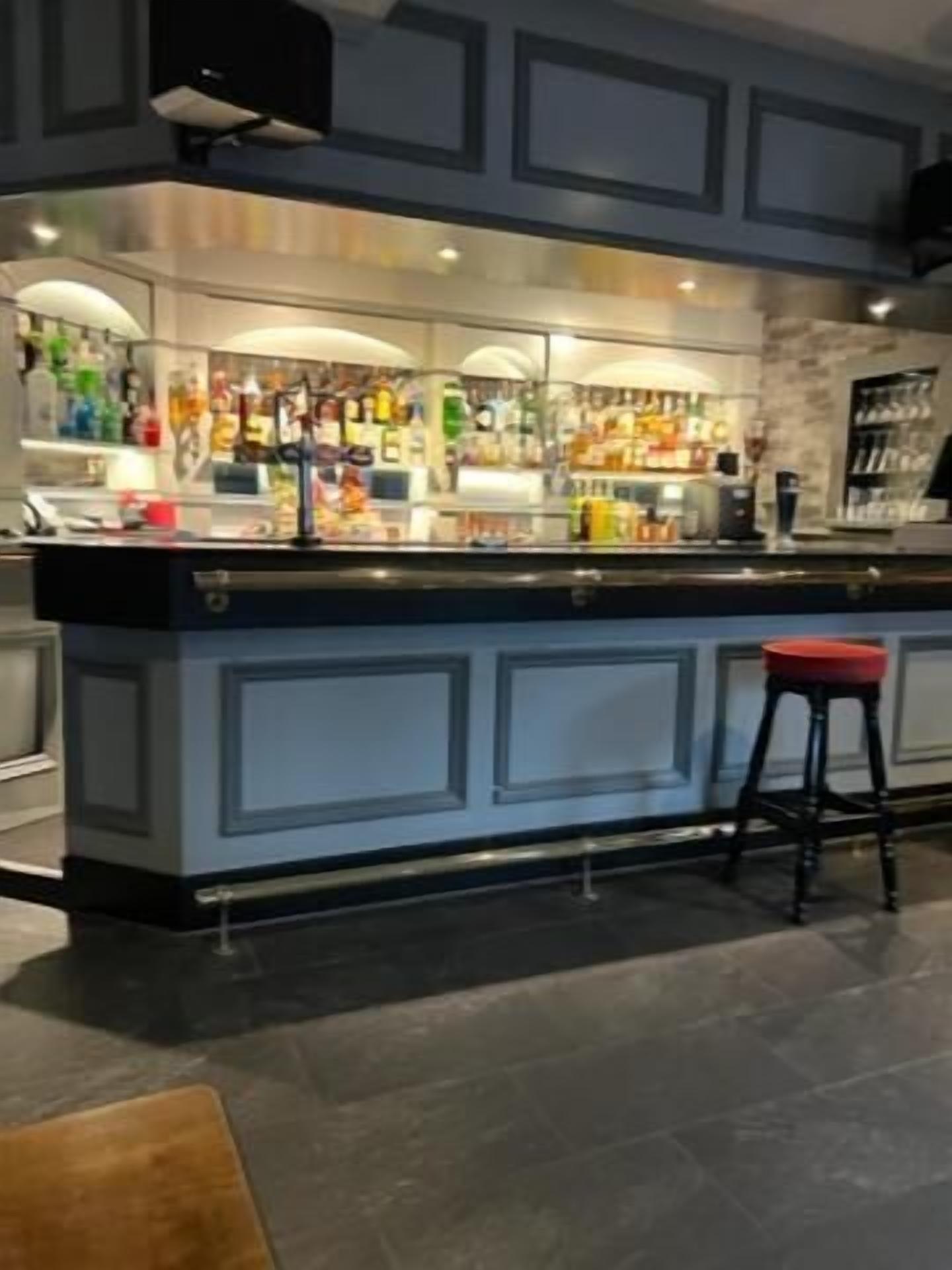 A bar area with a counter, stools, and a variety of bottles and glasses.