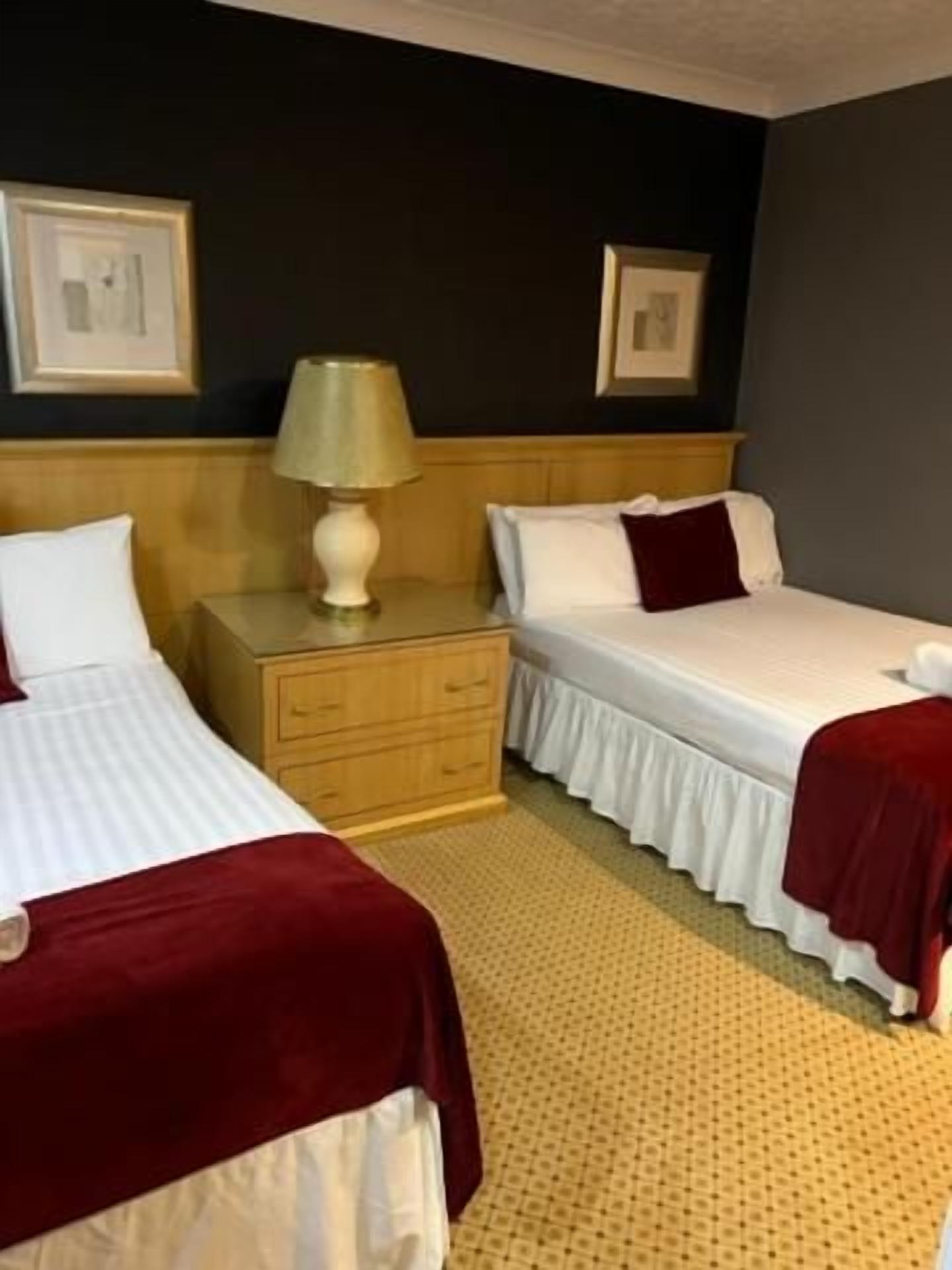 A hotel room with two beds, a nightstand, and a lamp.