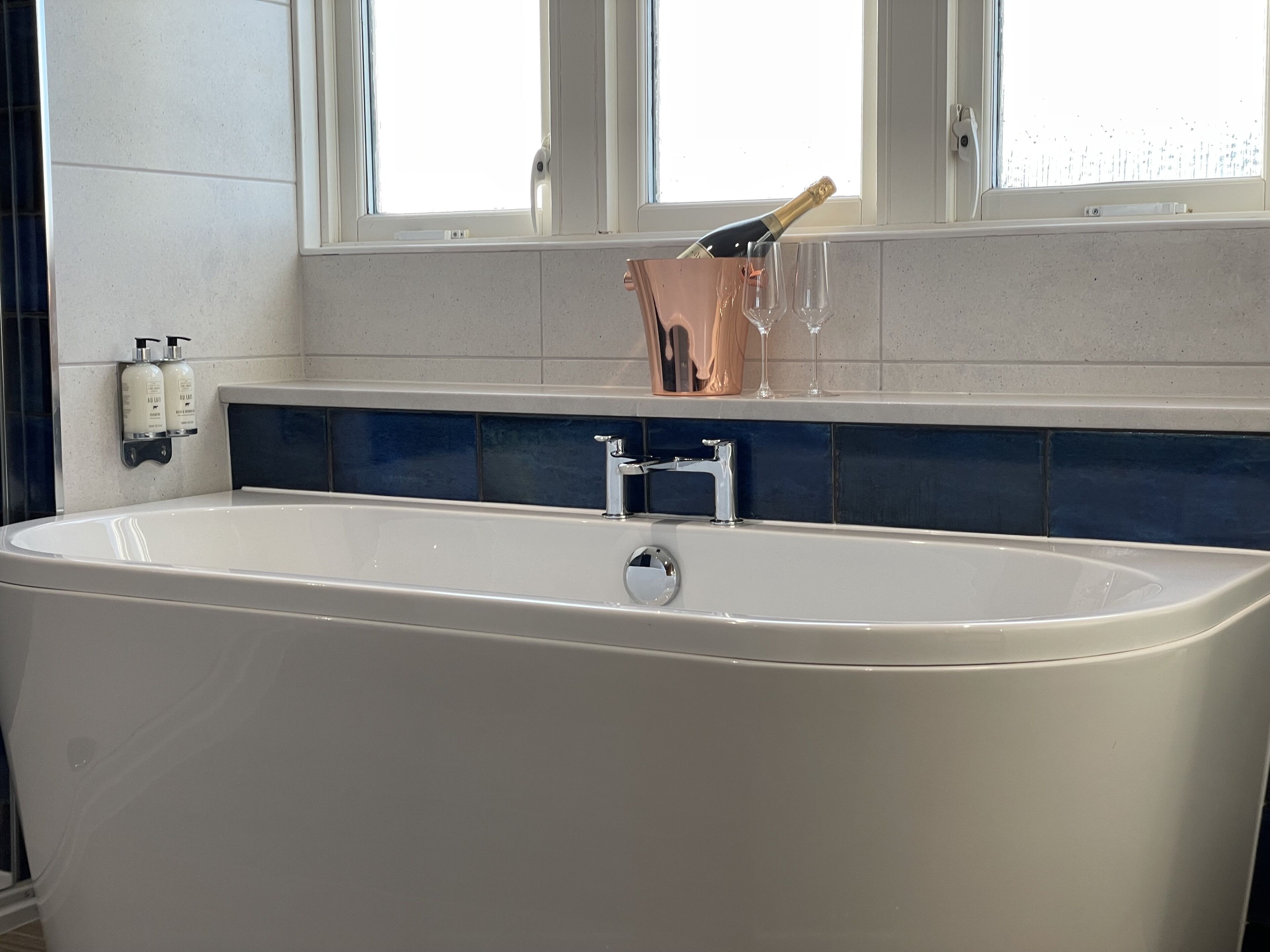 Une salle de bain moderne avec une baignoire sur pieds, une fenêtre au-dessus et un pare-baignoire bleu.