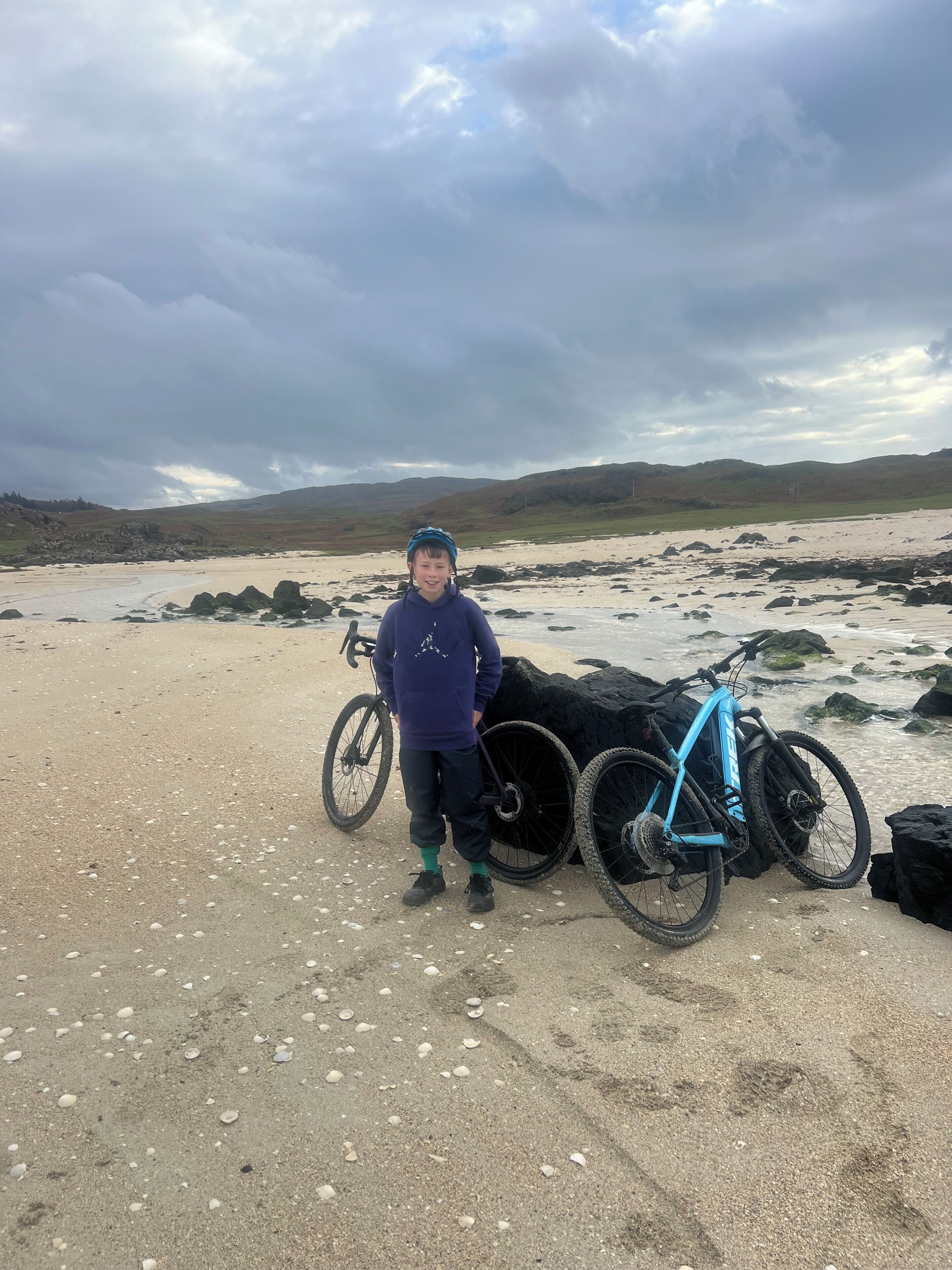 A person standing on a sandy beach with a bicycle.