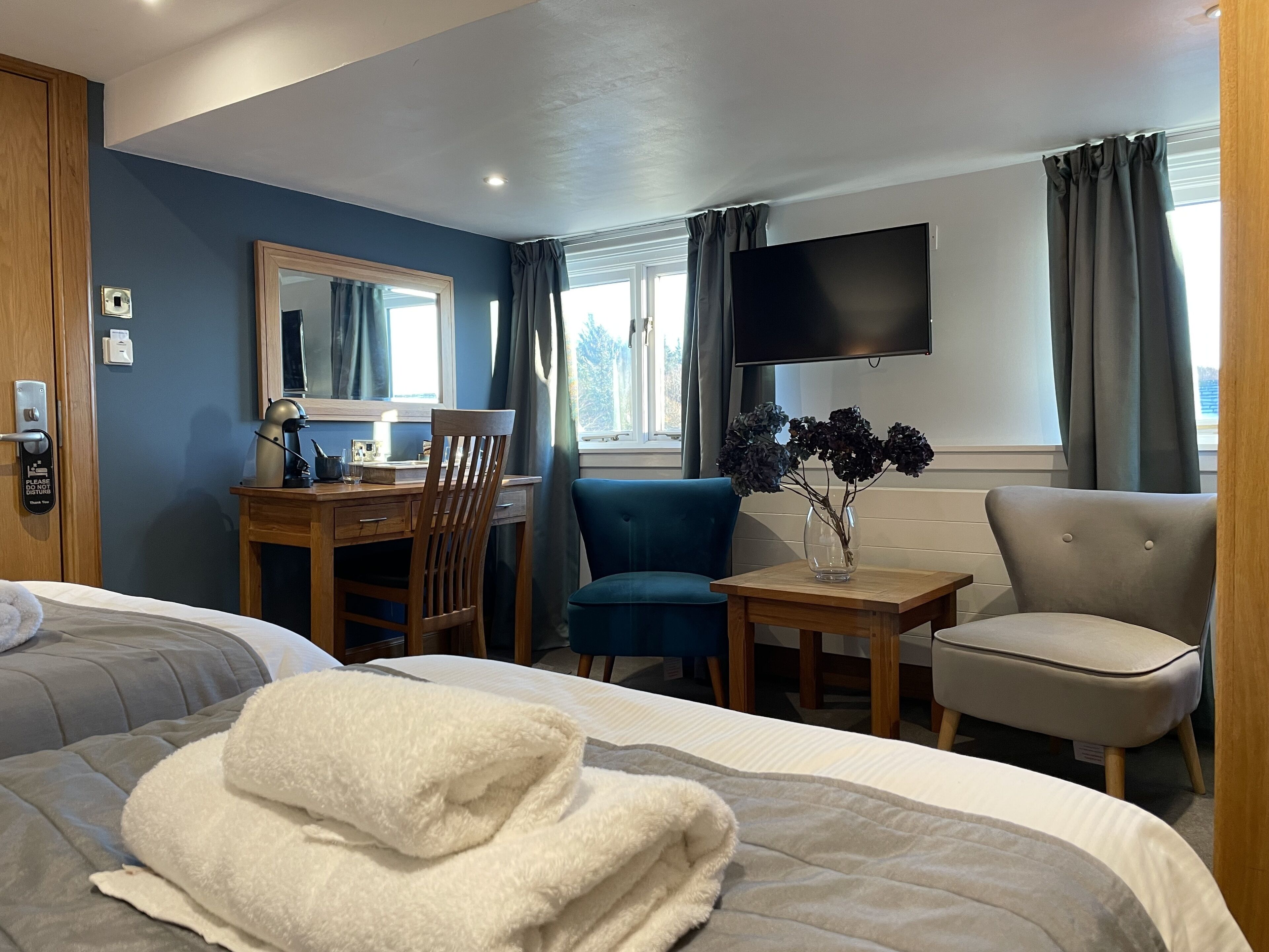 A hotel room with a bed, a desk, a chair, a TV, and a window with curtains.