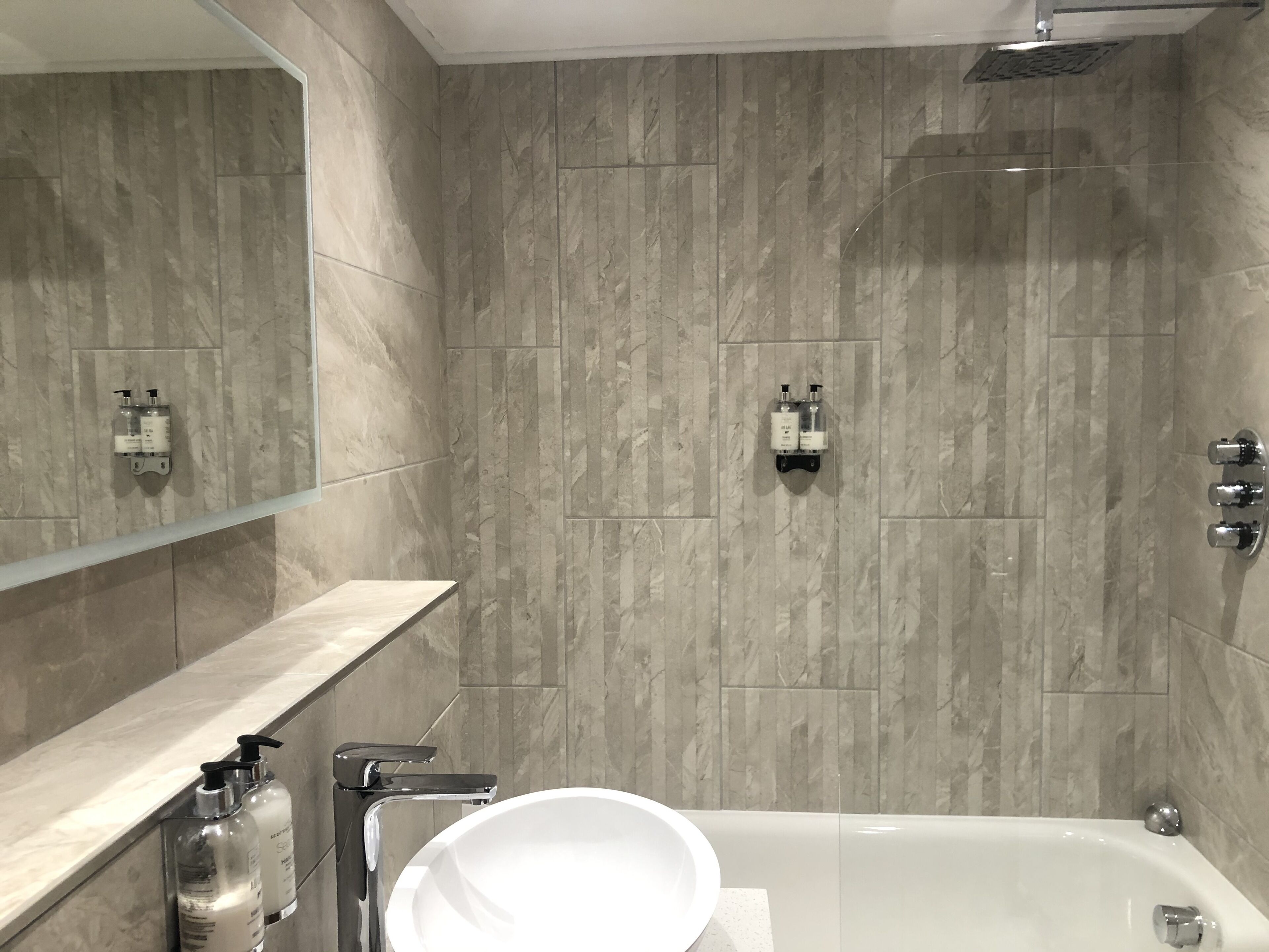A modern bathroom with a bathtub, a mirror, and two wall-mounted soap dispensers.