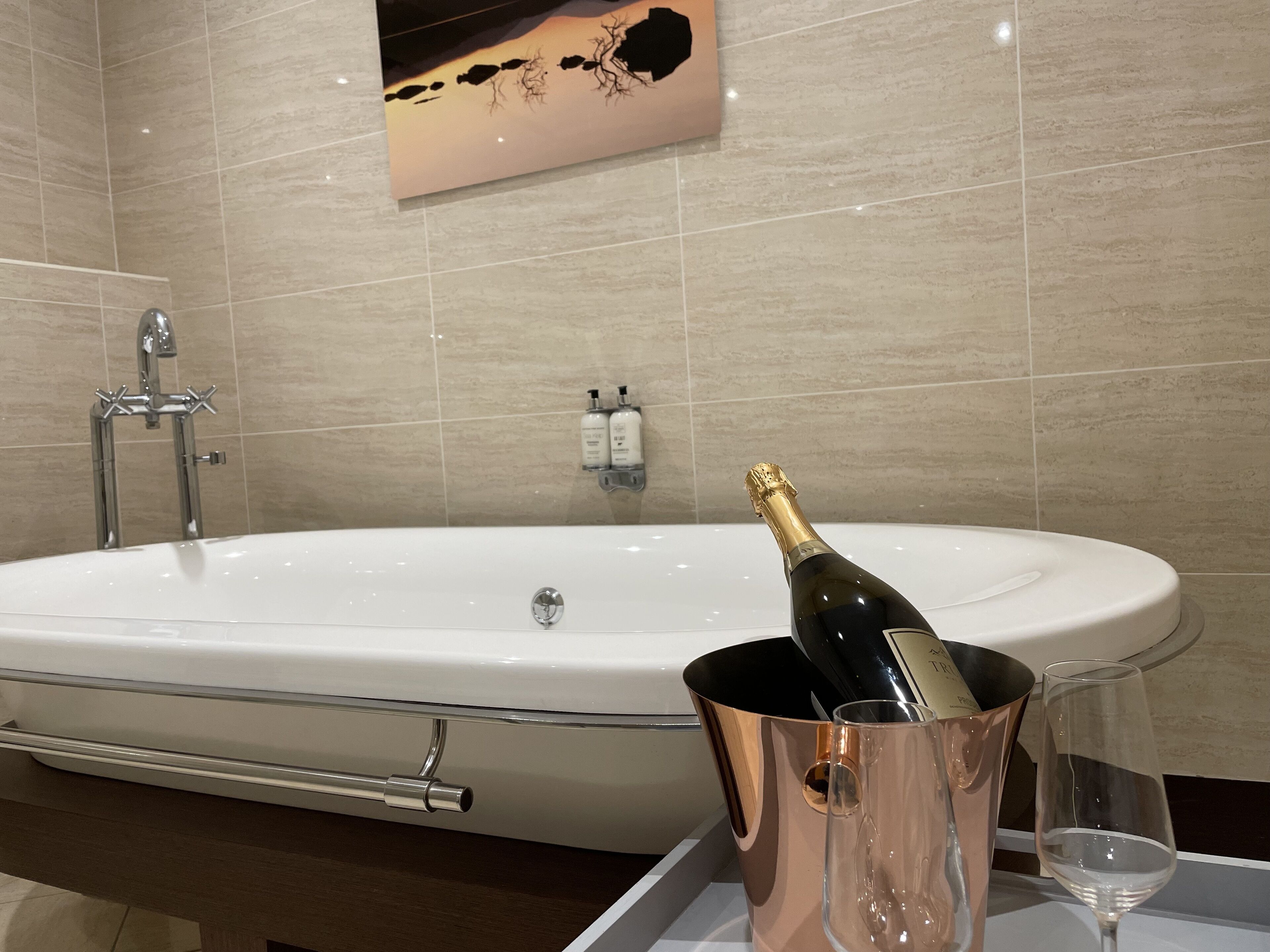 A modern bathroom with a large bathtub, a champagne bottle in a copper bucket, and a glass on a tray.