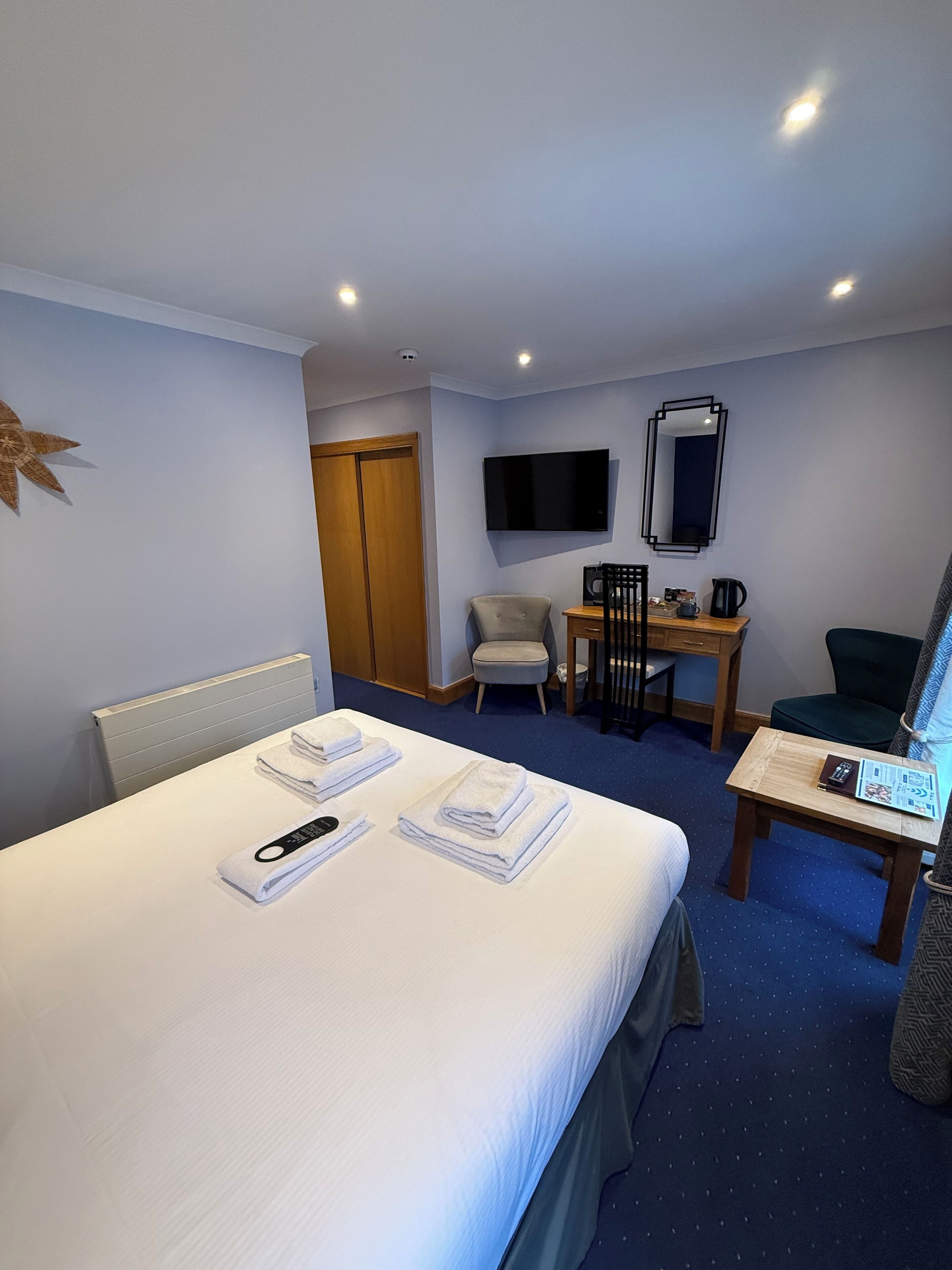 A hotel room with a bed, a desk, a chair, a TV, and a mirror.