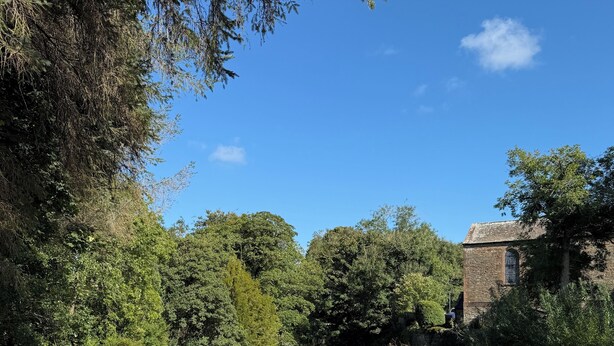 A serene riverside scene with lush greenery, a calm water body reflecting the sky, and a historic building in the background. - The Ship Inn (Castle Douglas)