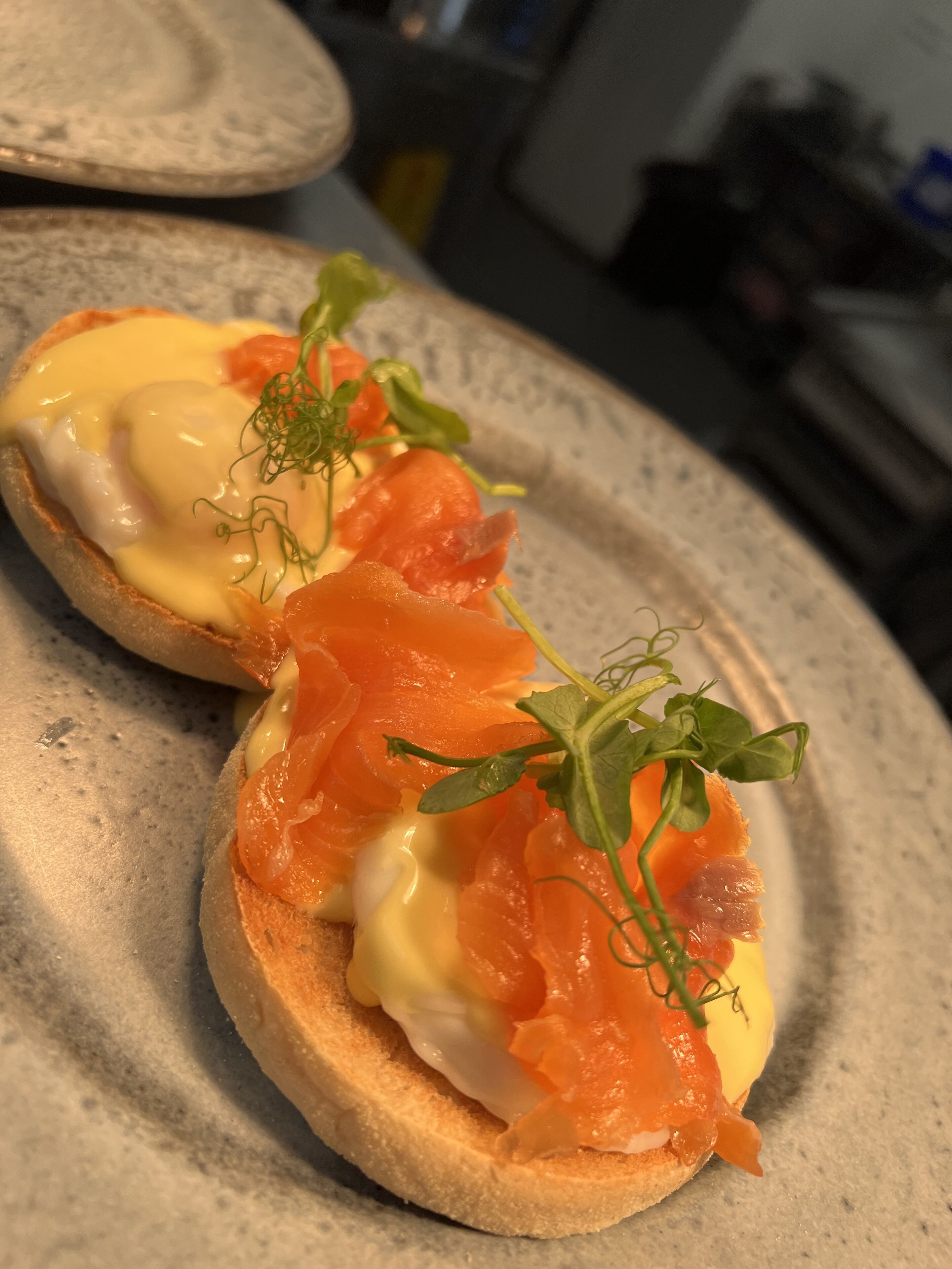 A plate with two open-faced sandwiches topped with smoked salmon and hollandaise sauce, garnished with microgreens.