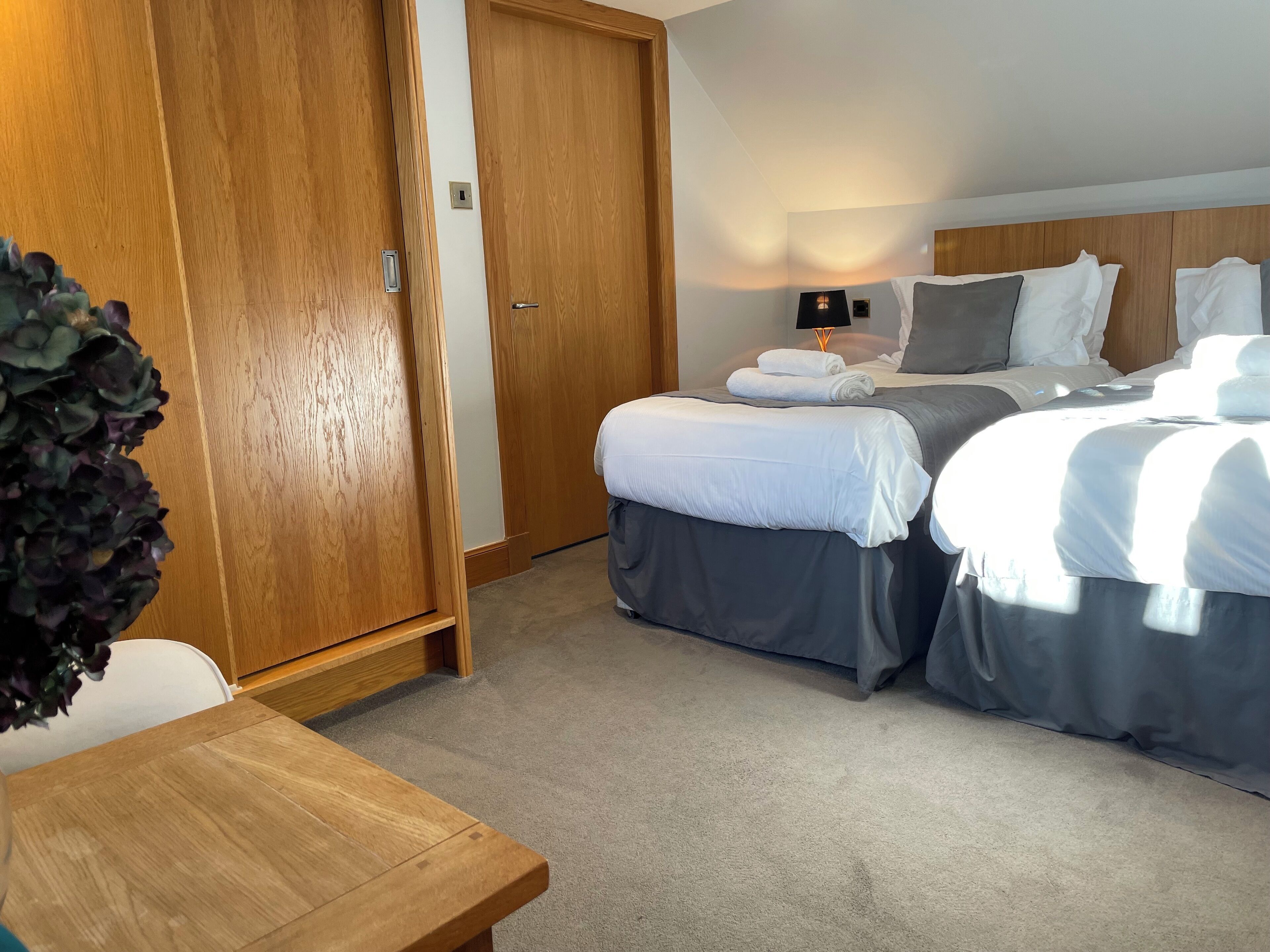 A hotel room with a wooden wardrobe, a bed with white bedding, a bedside table, and a lamp.