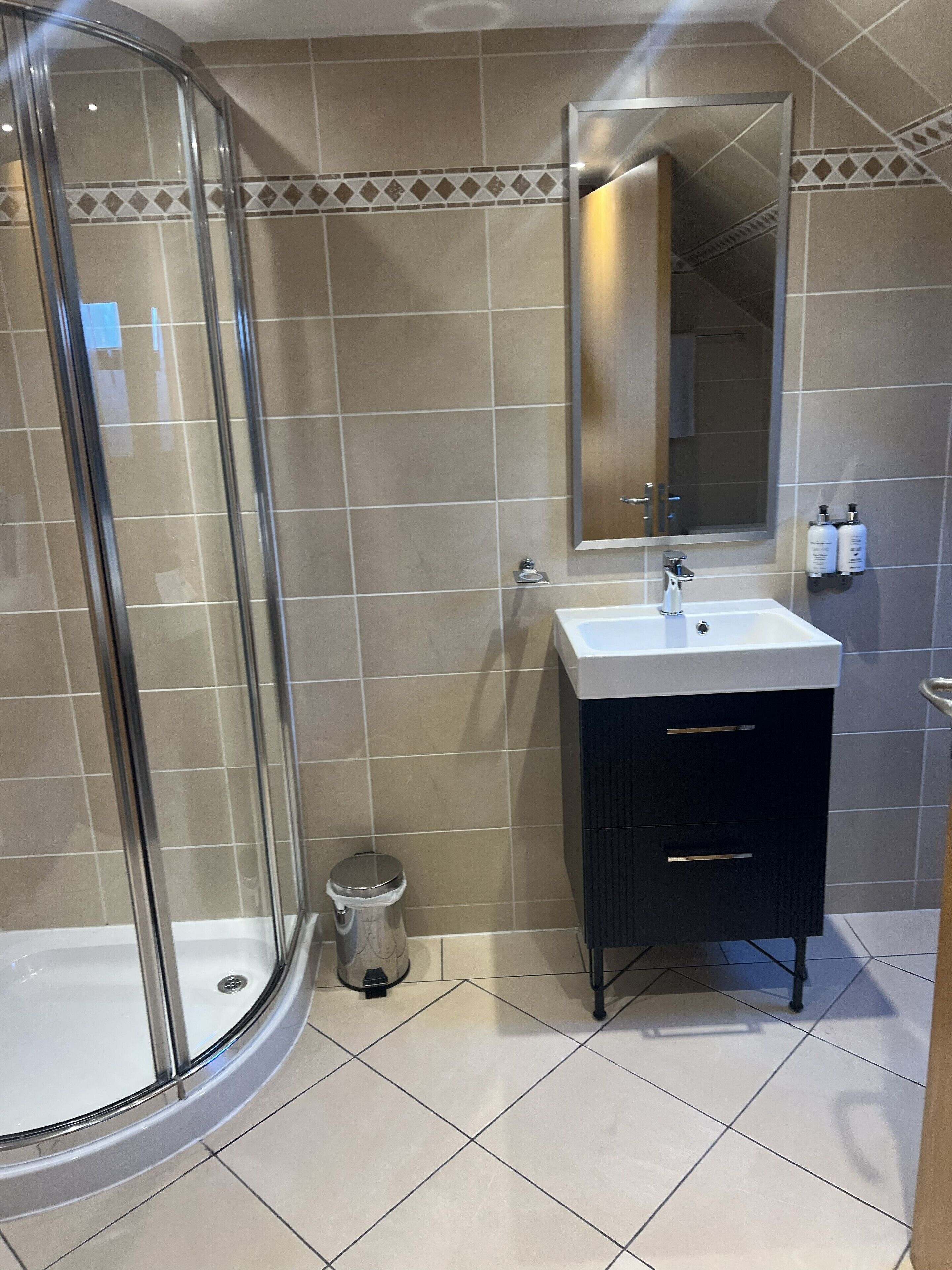 A modern bathroom with a glass shower enclosure, a sink with a mirror, and a vanity with drawers.