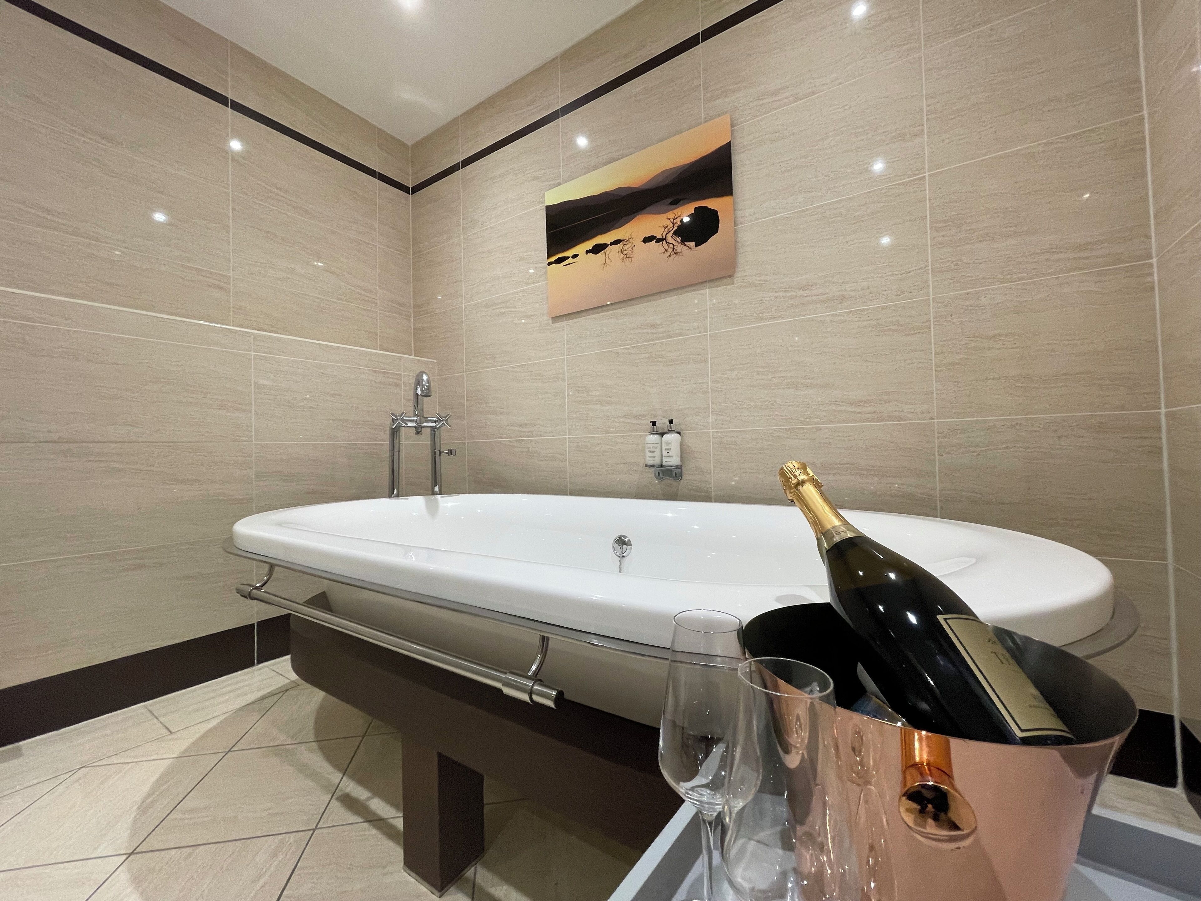 A modern bathroom with a large bathtub, a champagne bottle, and a glass.