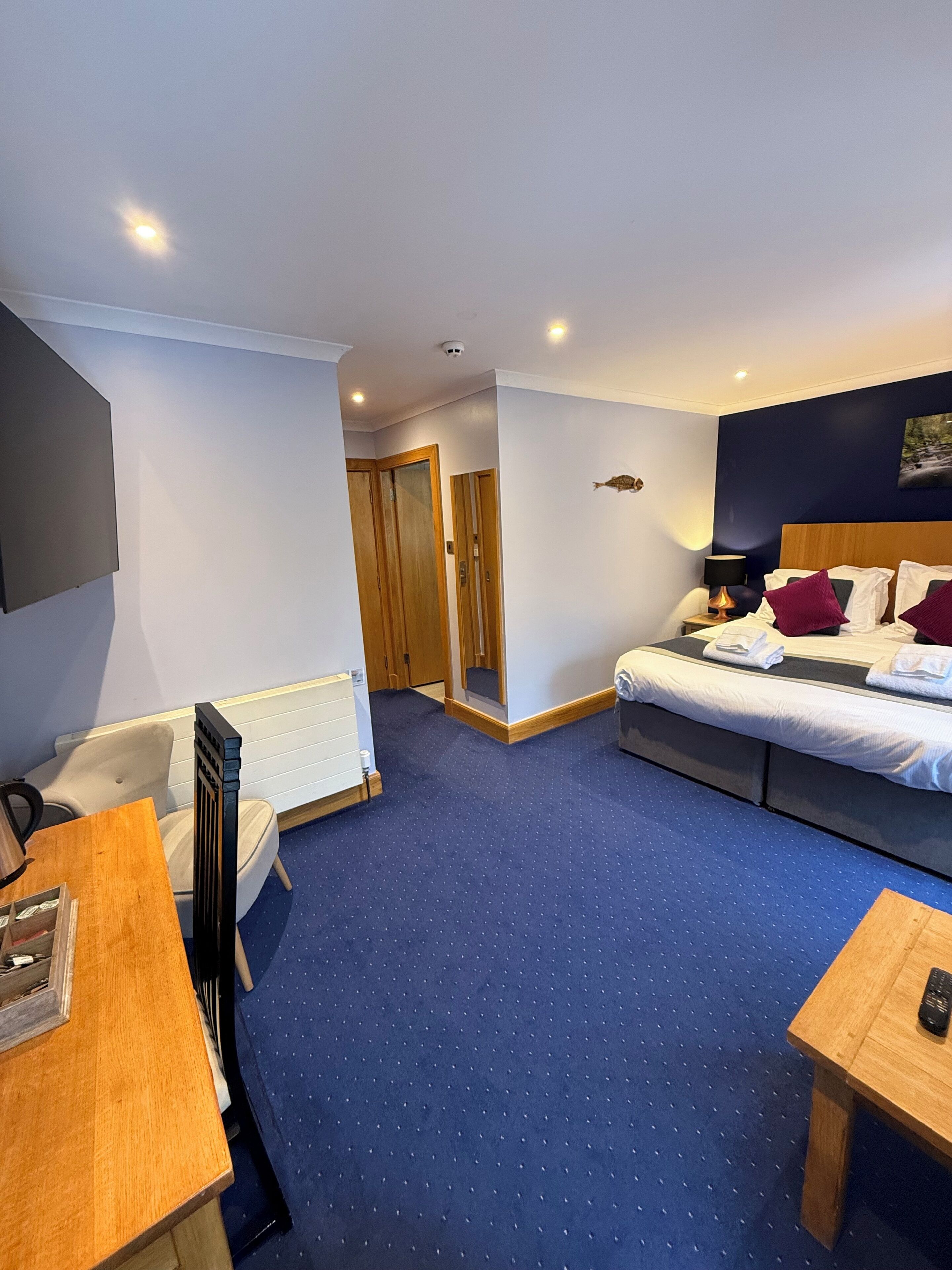 Een hotelkamer met een bed, een bureau, een stoel, een radiator en een aan de muur bevestigde televisie.