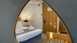 A hotel room with a bed, a bedside table with a lamp, a wooden chair, and a door with a sign. - The Ship Inn (Castle Douglas)