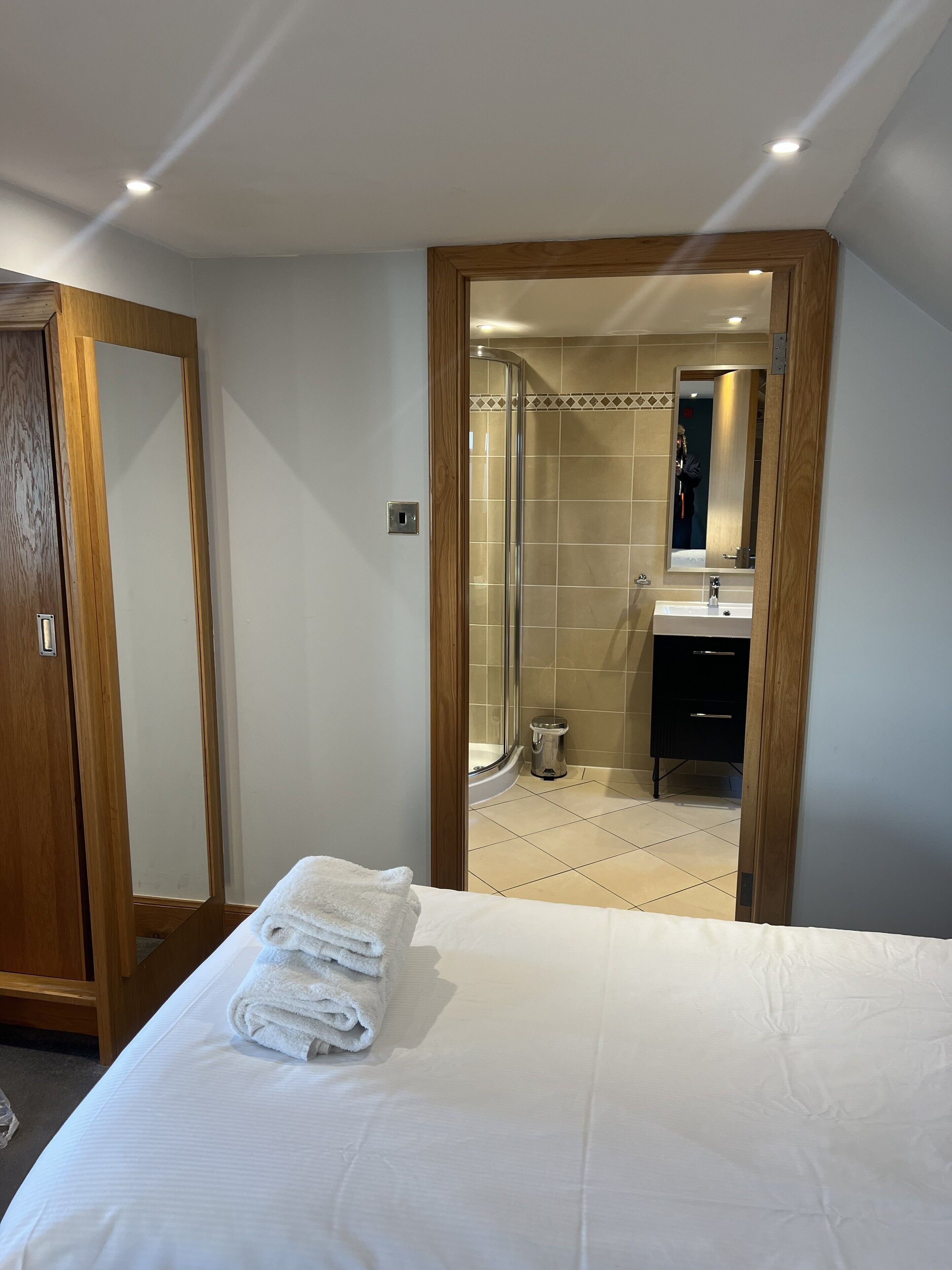 A hotel room with a neatly made bed, a wooden wardrobe, and a bathroom visible through an open door.
