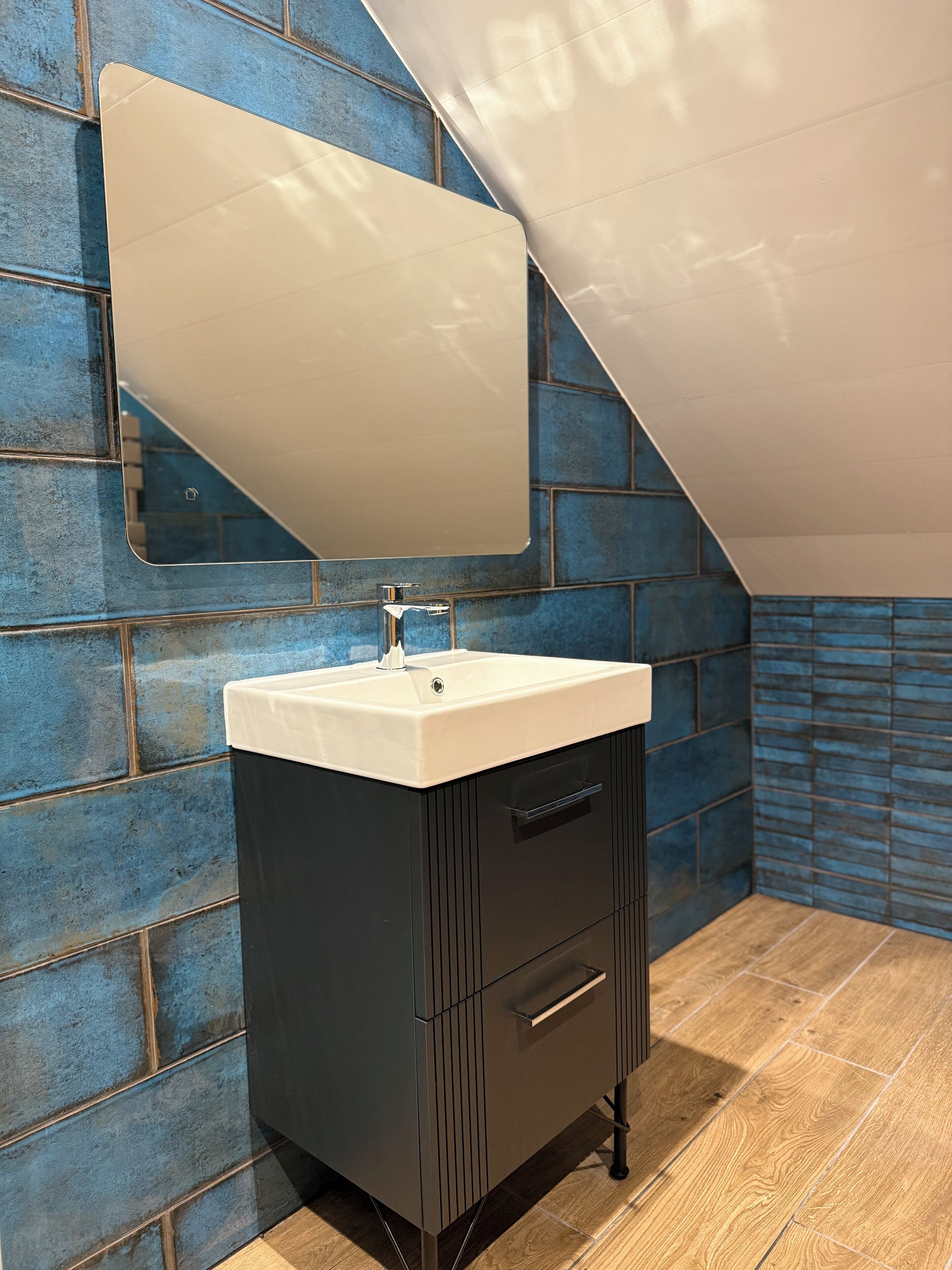 A bathroom with a white sink, dark cabinetry, and a blue-tiled wall.