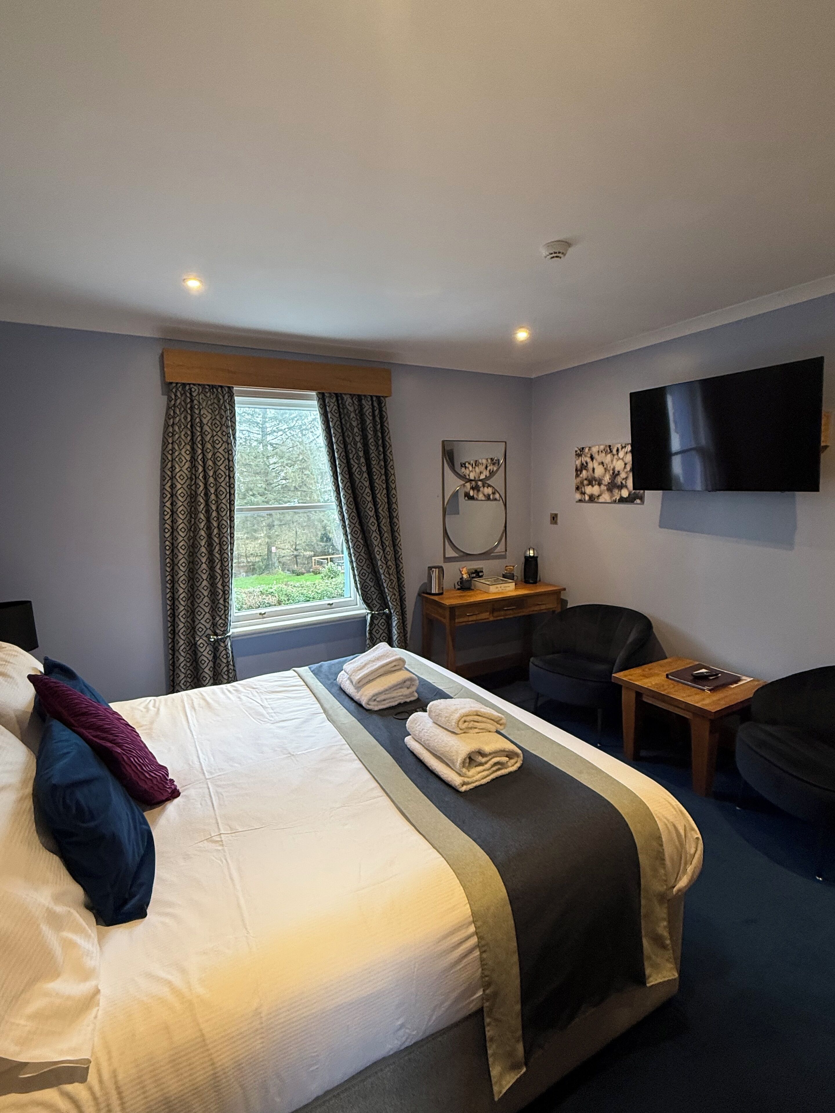 Une chambre d’hôtel avec un grand lit, un bureau, une chaise, une télévision et une fenêtre avec des rideaux.