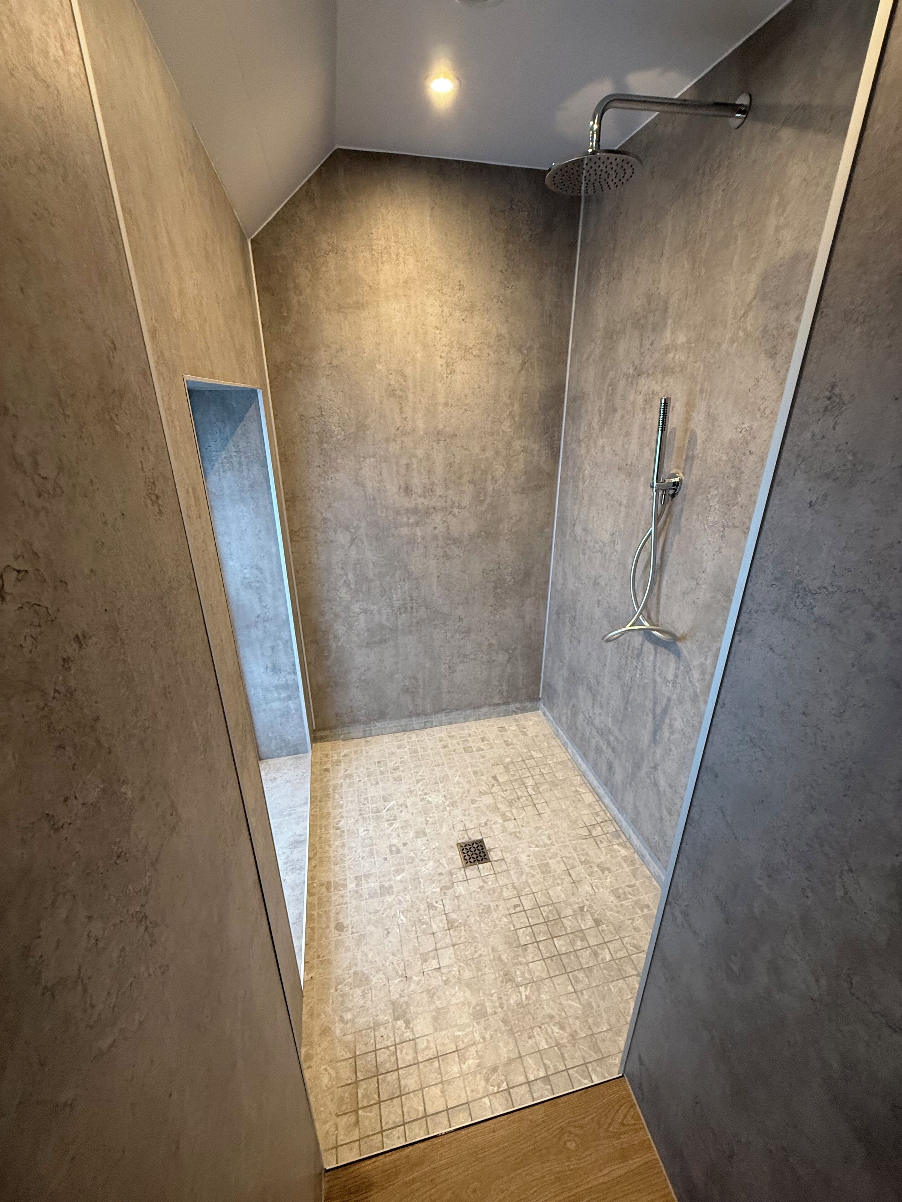 A modern shower room with a glass door, a handheld showerhead, and a floor drain.