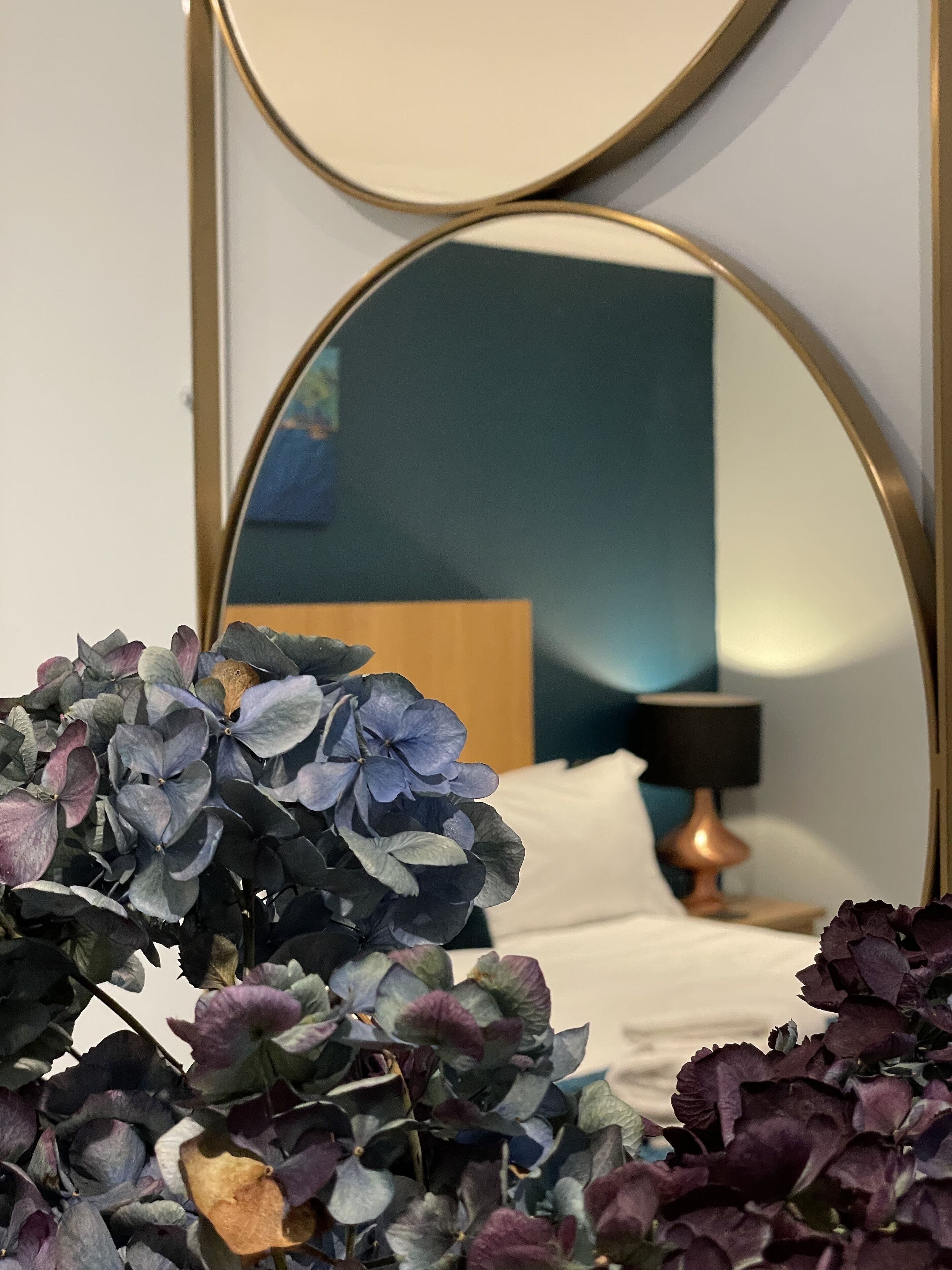 Quarto com um espelho grande, cama com roupa de cama branca, cabeceira de madeira e luminária de cabeceira.
