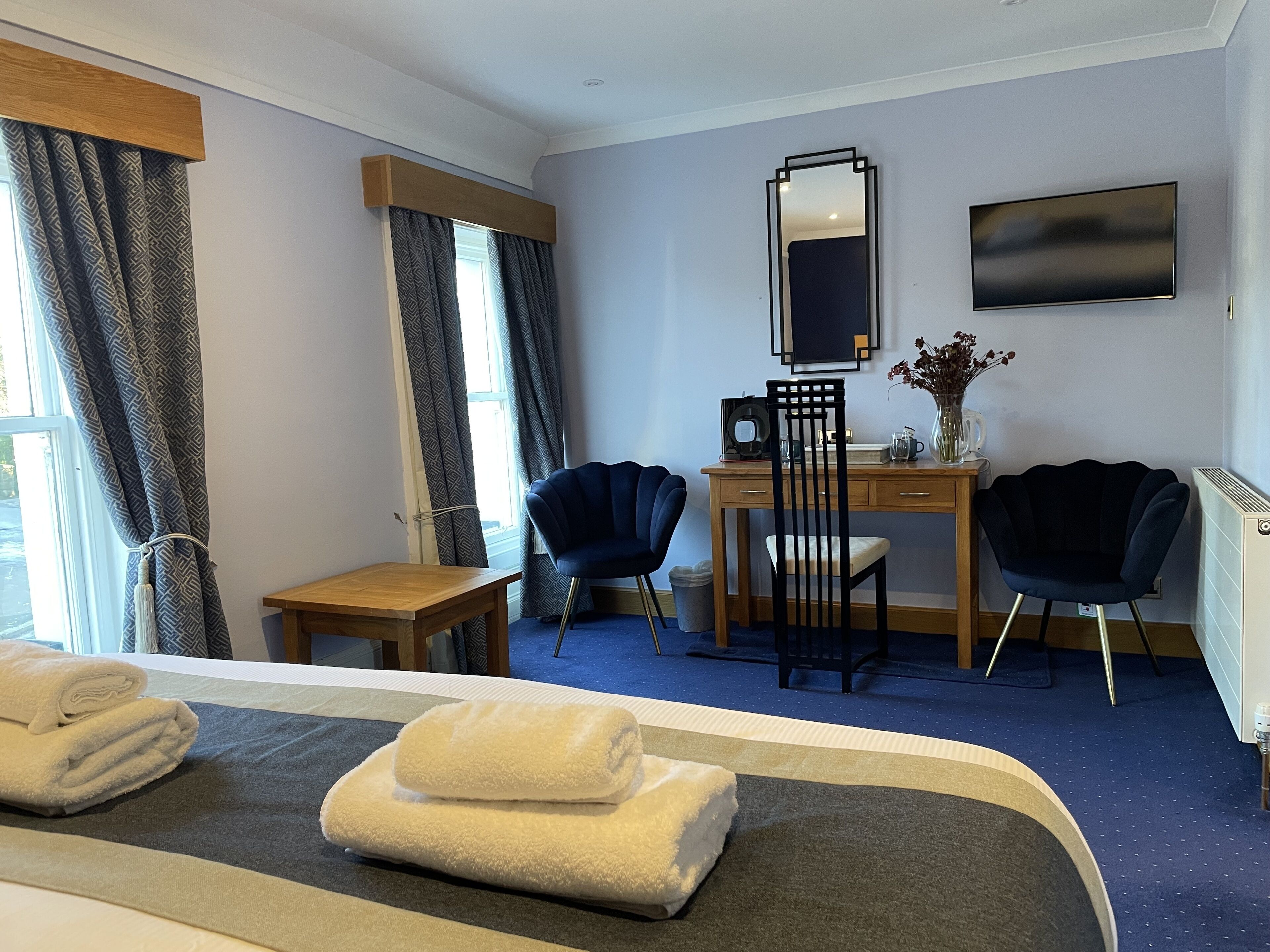 A hotel room with a bed, two chairs, a desk, a mirror, and a TV.