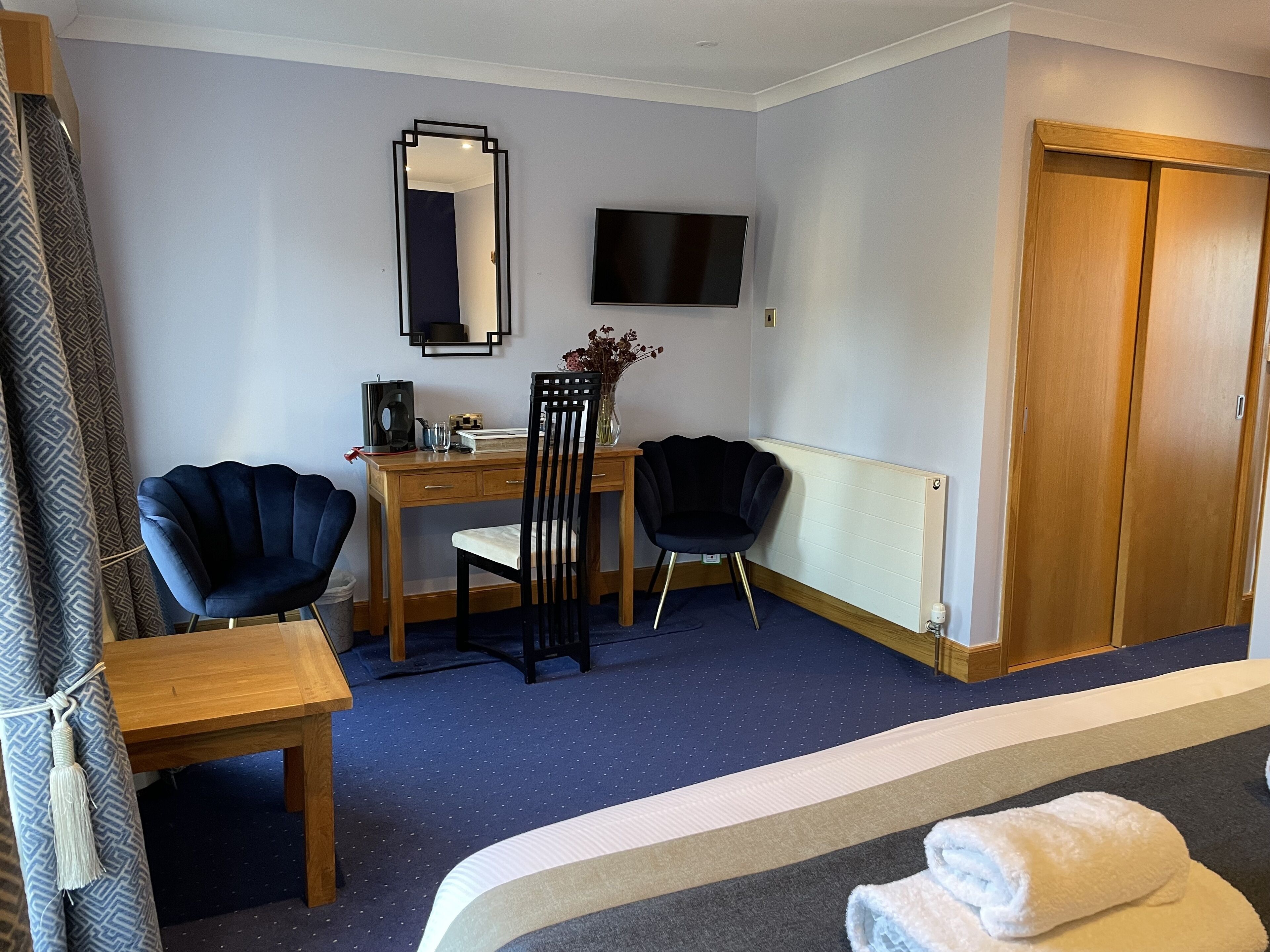 Ein Hotelzimmer mit Bett, Schreibtisch, zwei Stühlen, Fernseher und einem Holzschrank.