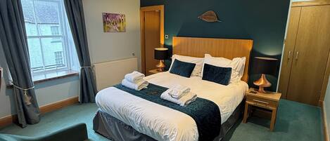A neatly arranged hotel room with a bed, a chair, a nightstand, and a wardrobe.
